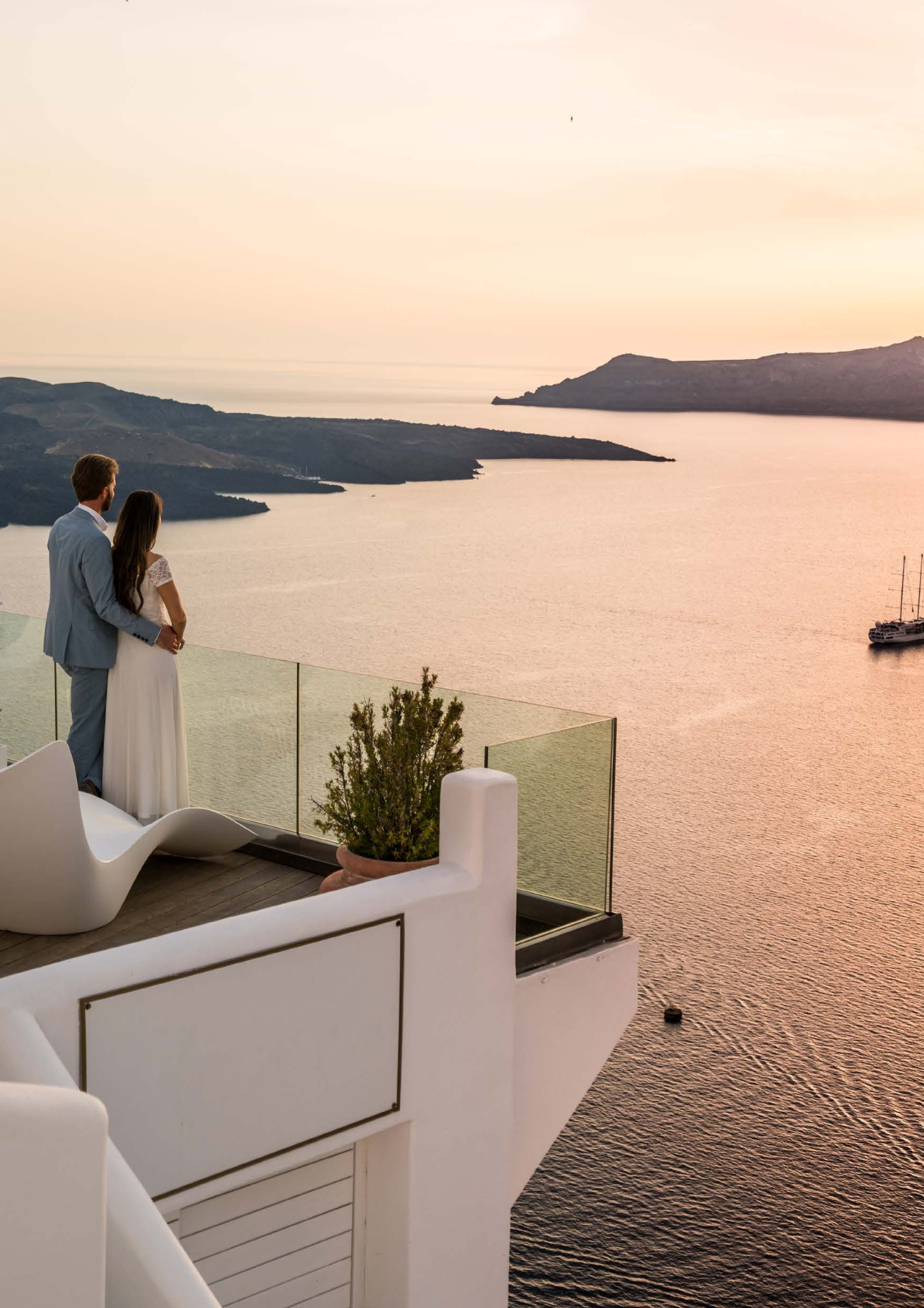 net getrouwd paar kijkt vanaf hotel uit over de inham van een zee met de ondergaande zon