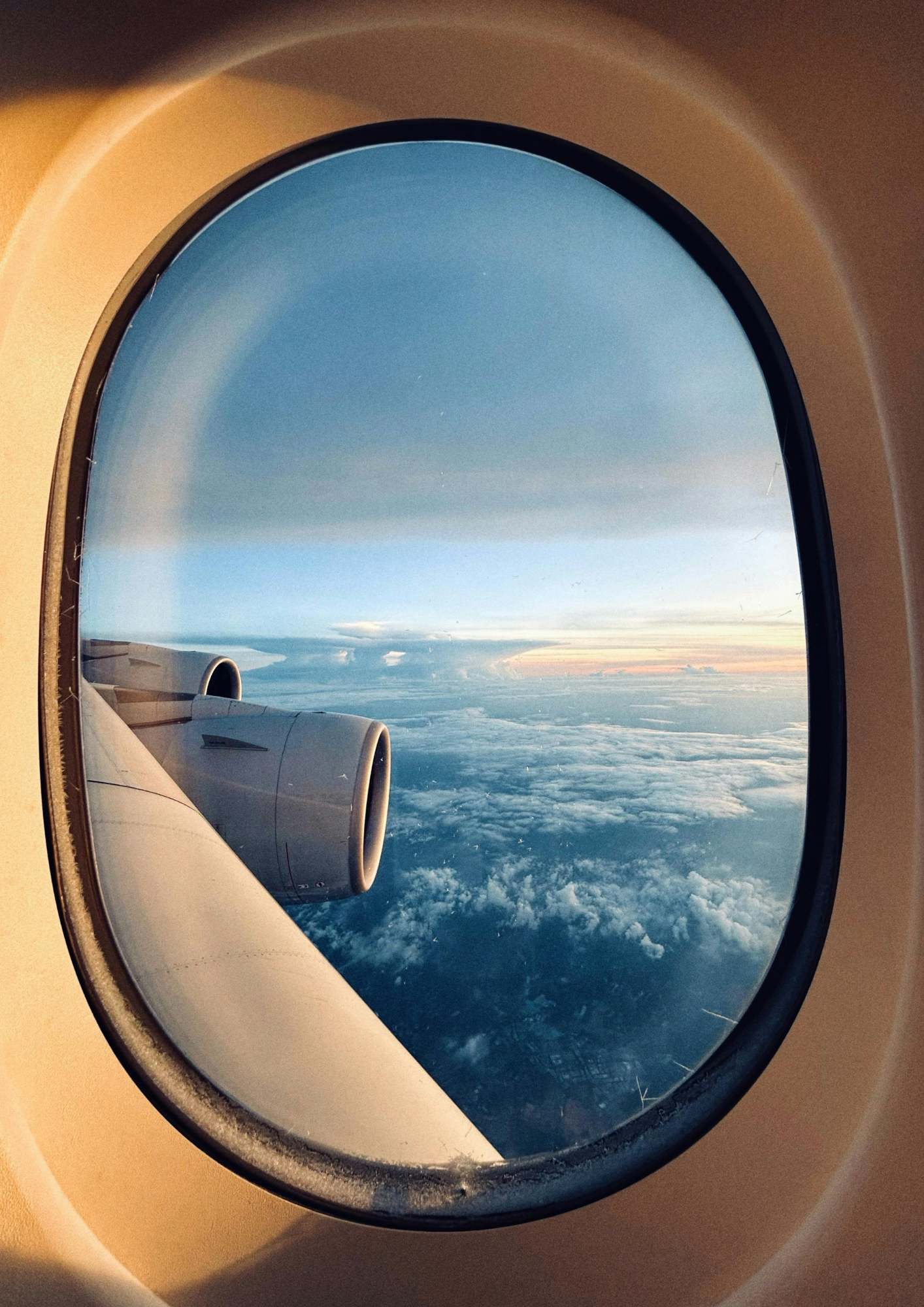 Uitzicht uit een vliegtuigraam met een motor, wolken en de avondlucht.