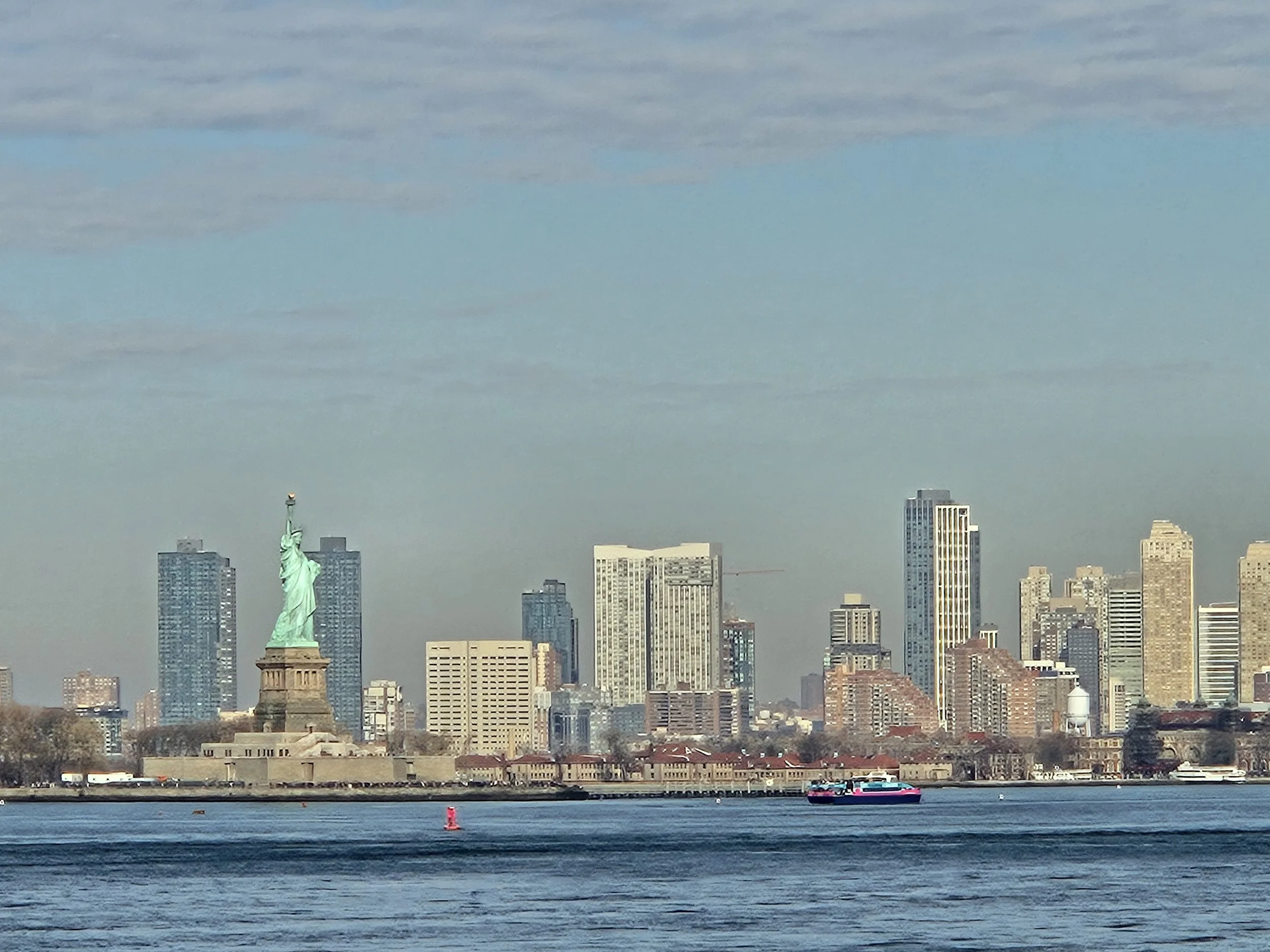 Zicht op de skyline van New York City met het Vrijheidsbeeld op de voorgrond en wolkenkrabbers op de achtergrond, geschoten vanaf het water.
