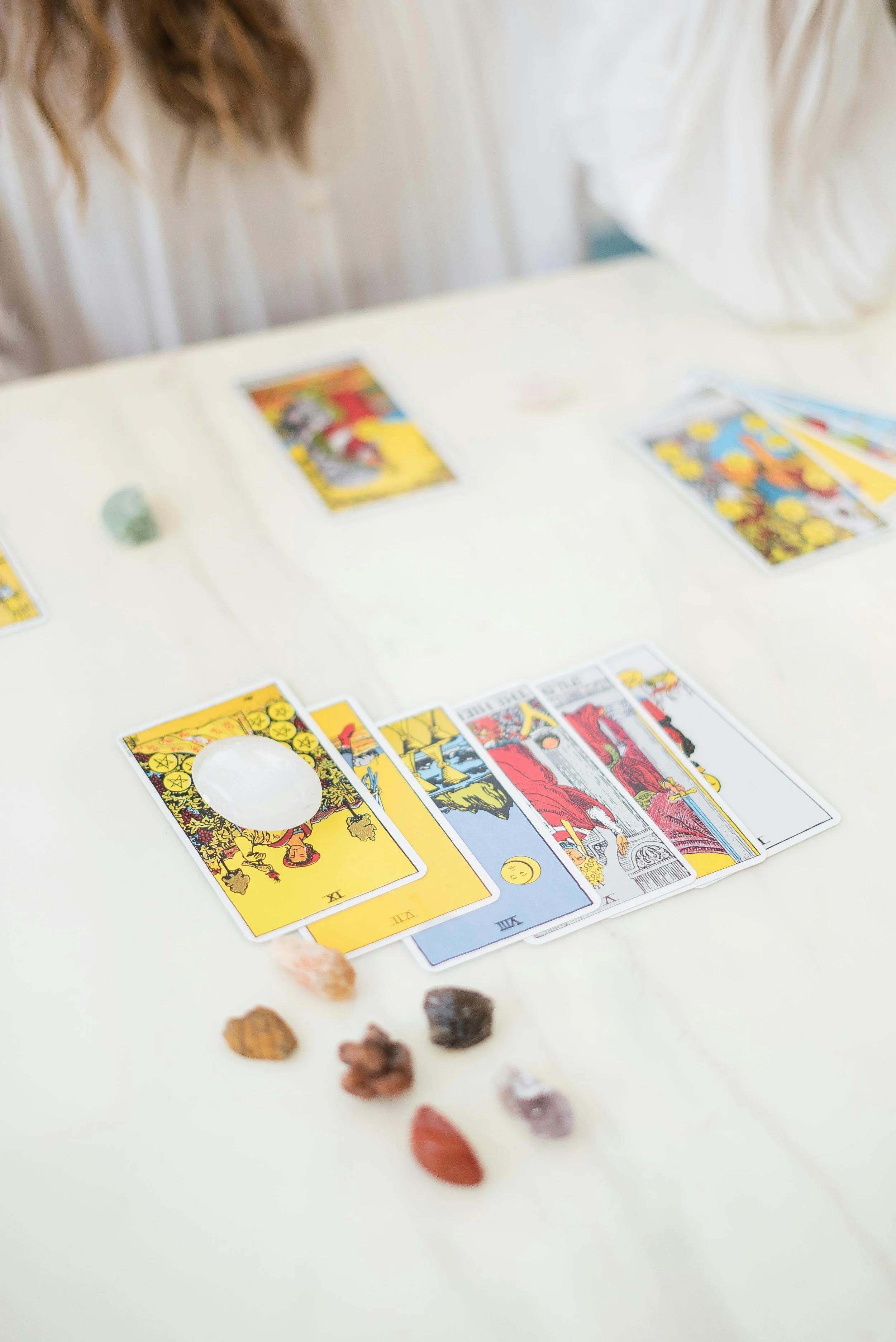 Jeu de tarot avec des cartes et des pierres colorées sur une table blanche.