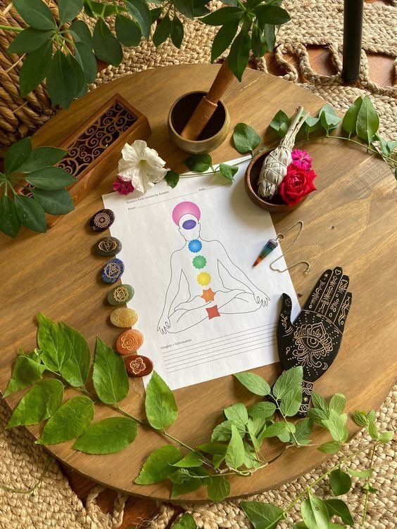 Table ronde en bois avec un dessin d'une silhouette humaine méditant, entourée de pierres colorées, feuilles vertes, et objets de méditation comme une encensoir, une main en bois sculptée, et des fleurs.