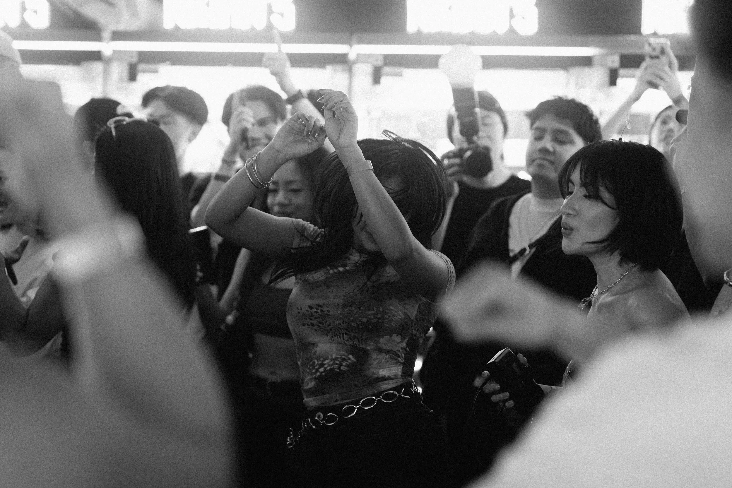 A crowd of people dancing and enjoying themselves at an event, with some holding cameras and phones, in a lively atmosphere.