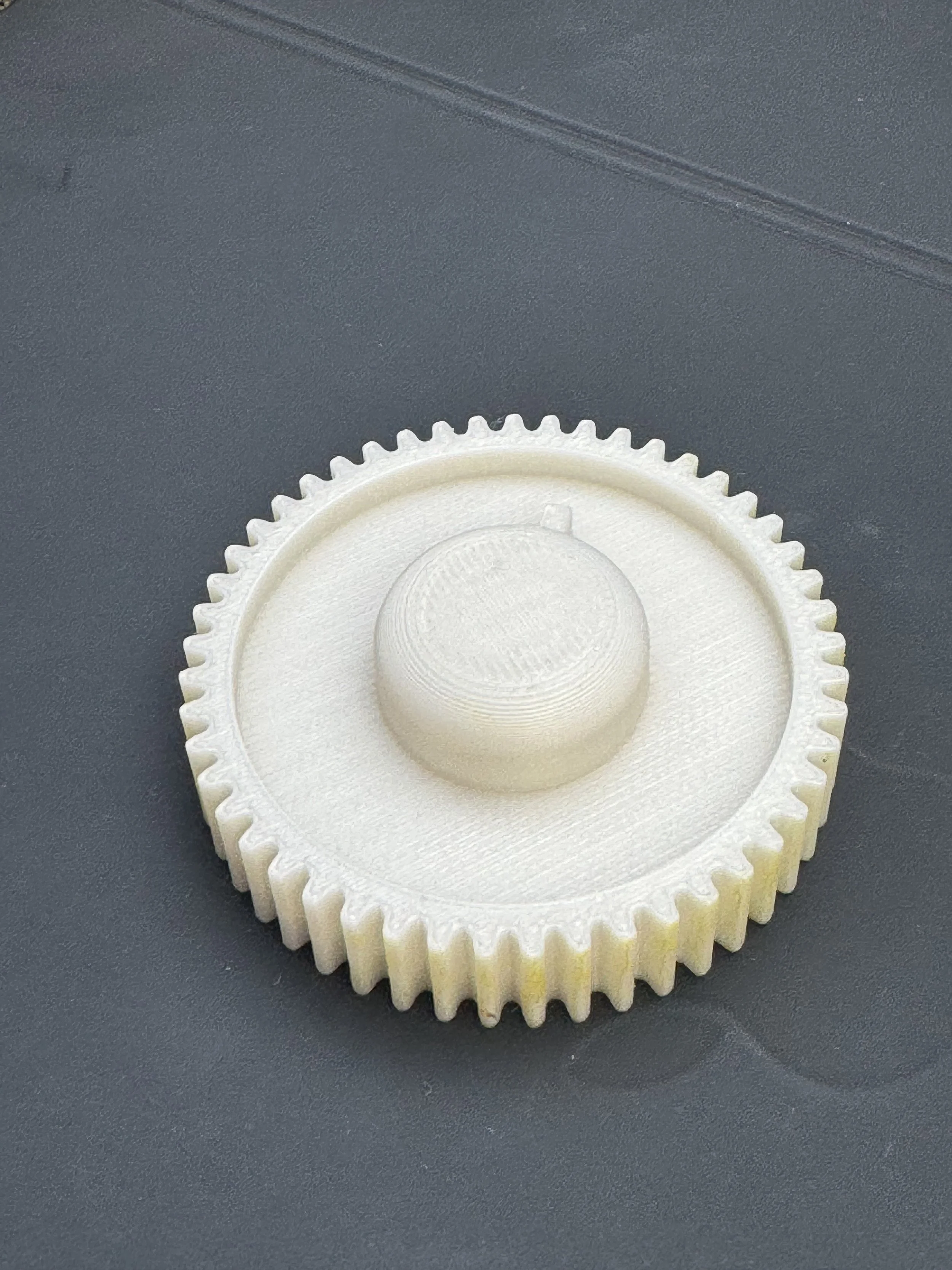 3D-printed white gear with a central knob on a gray surface.