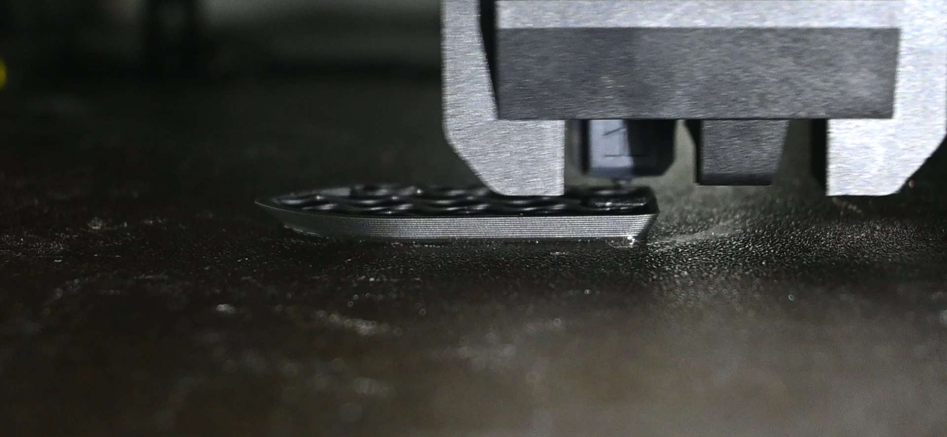 Close-up of a 3D printer's nozzle extruding filament onto a heated build plate.
