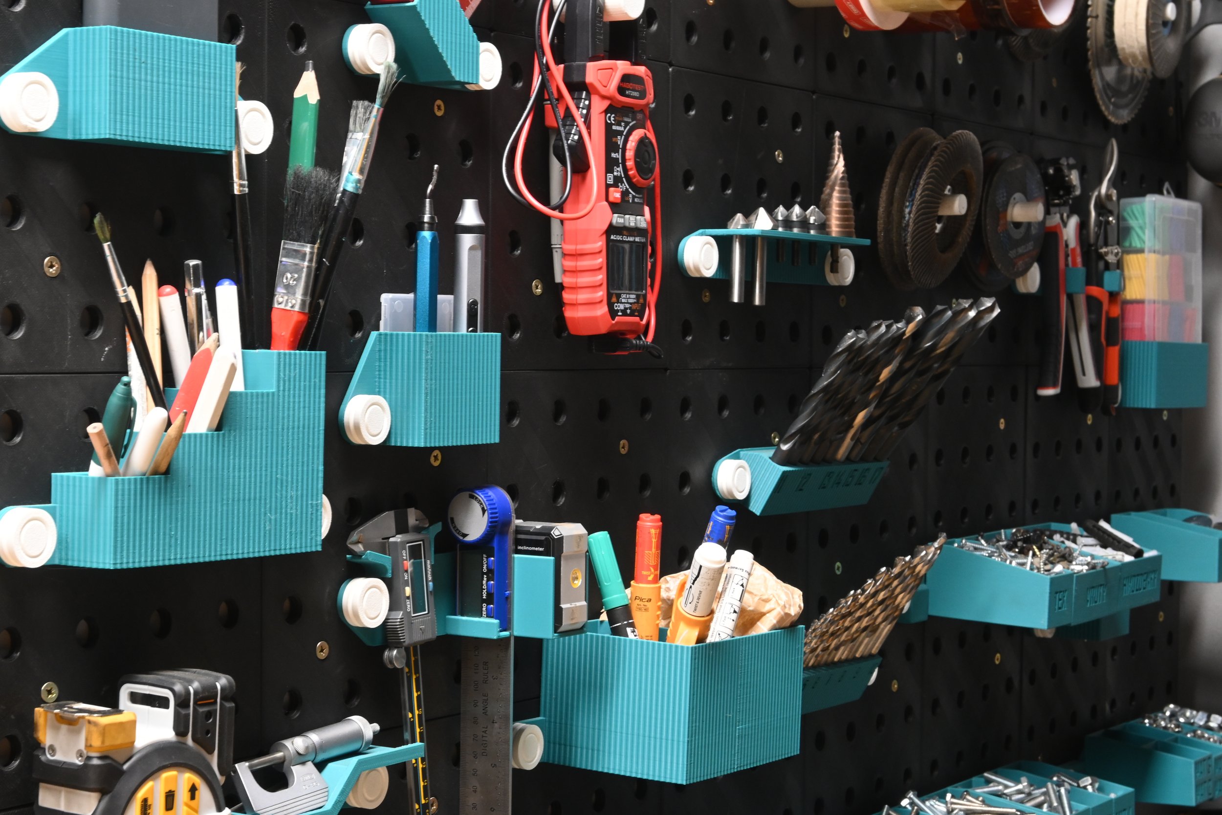 A pegboard filled with various tools and supplies, including paintbrushes, screwdrivers, drill bits, and measuring tools arranged in teal storage containers.