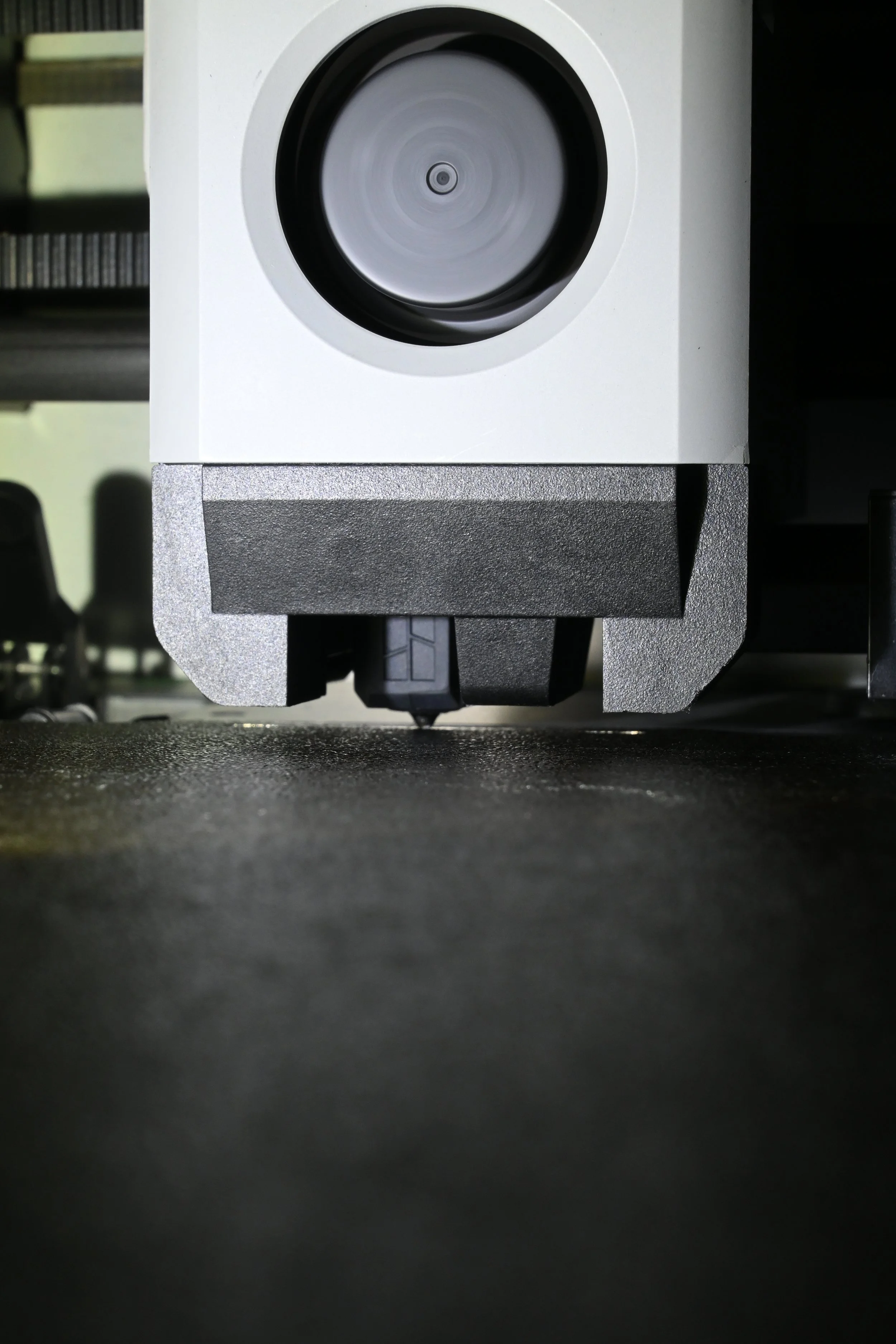 Close-up of a 3D printer's print head in action on a black printing surface.