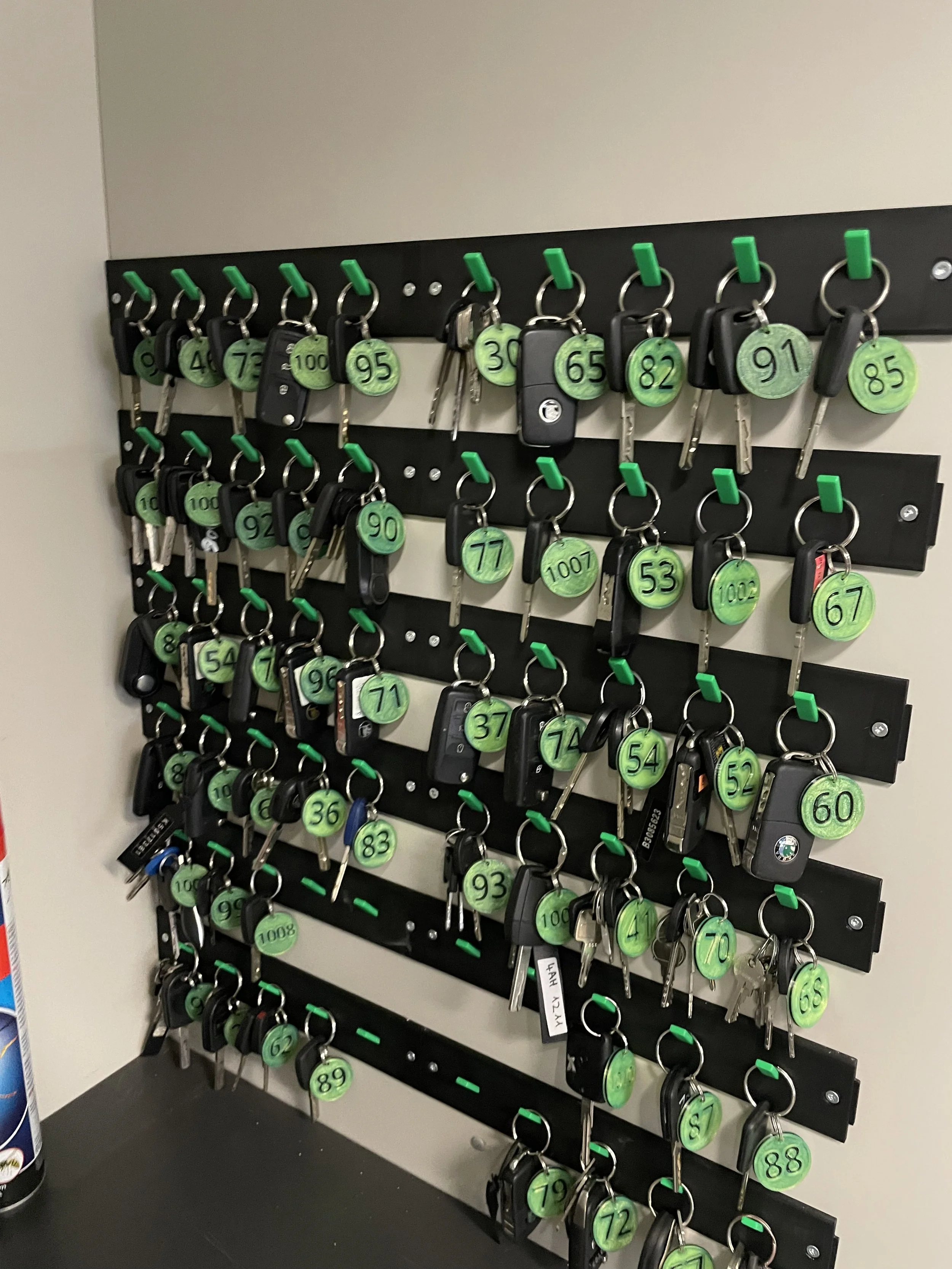 A wall-mounted rack holding multiple car keys on keychains, each labeled with a unique green band number.