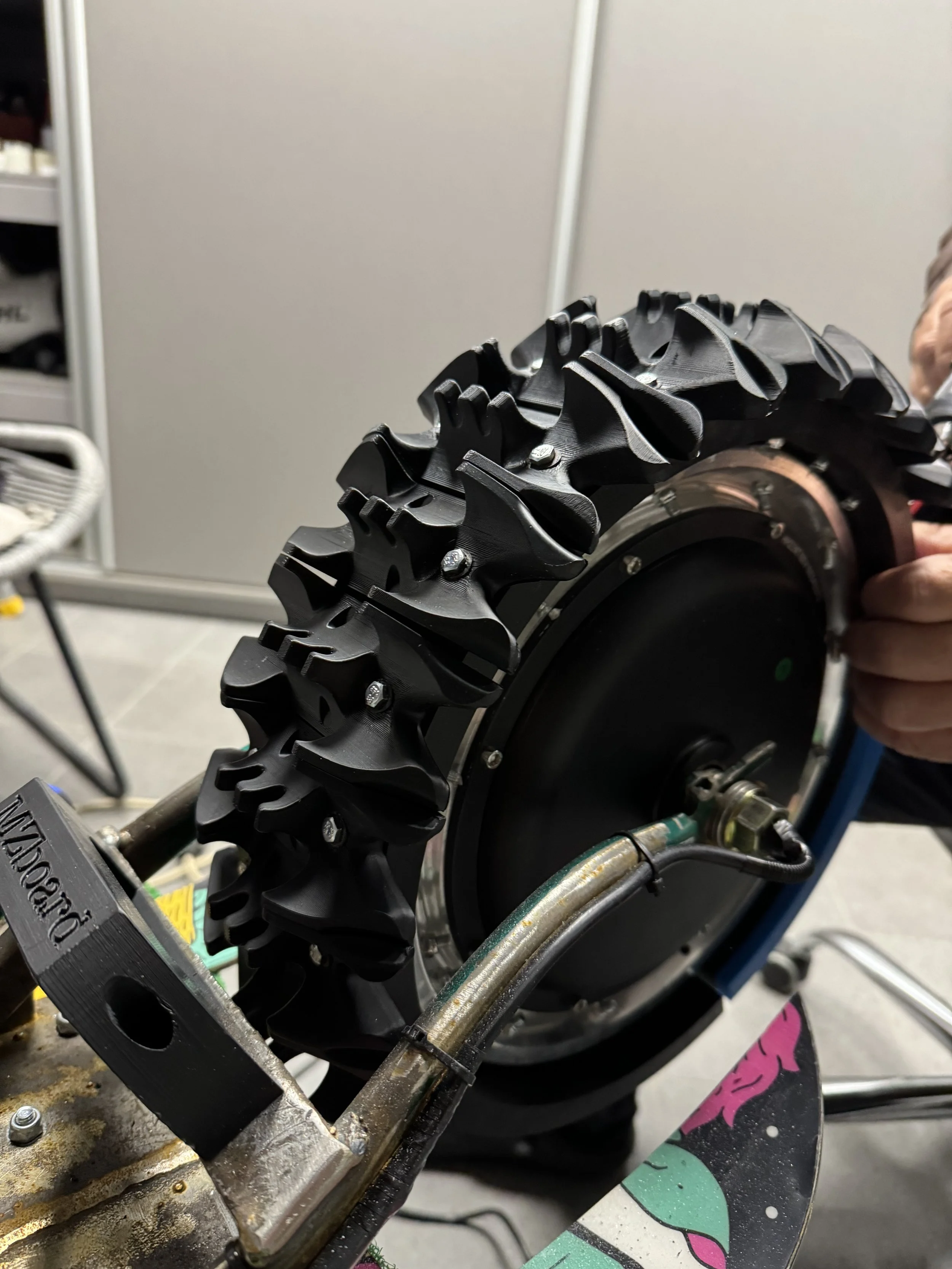 Close-up of a mechanical device with a black rubber tread, metal components, and bolts, possibly part of a tracked vehicle or machinery.