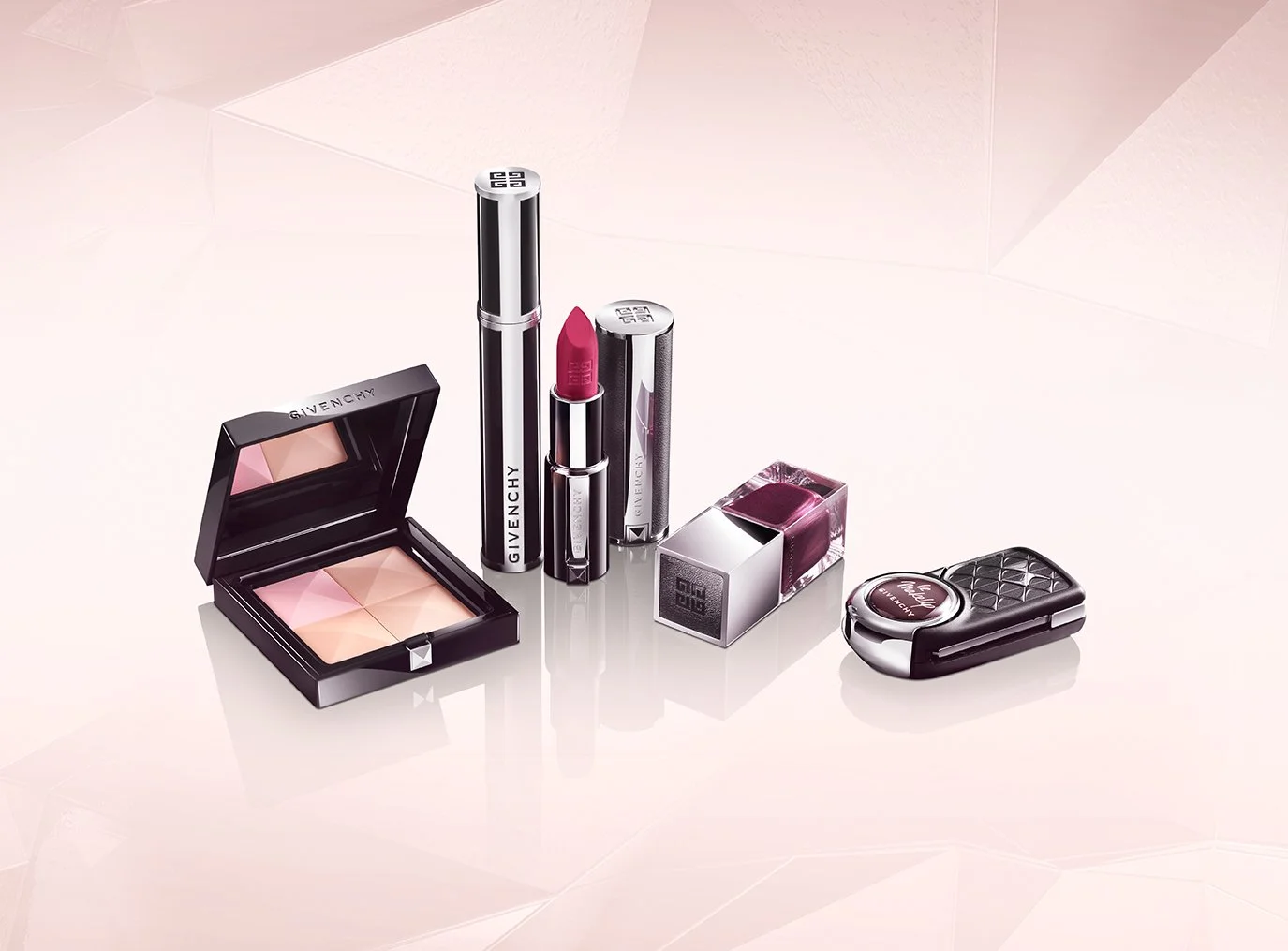 A collection of Givenchy beauty products including a powder compact, a lipstick, a perfume, a lip gloss, and a compact mirror, displayed on a light pink surface.