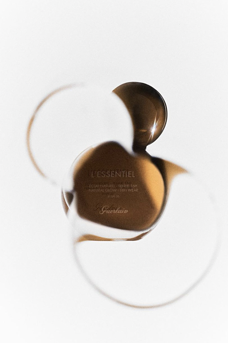A rolled-up bottle of Guerlain L'Essentiel natural glow foundation viewed through a reflecting sphere.
