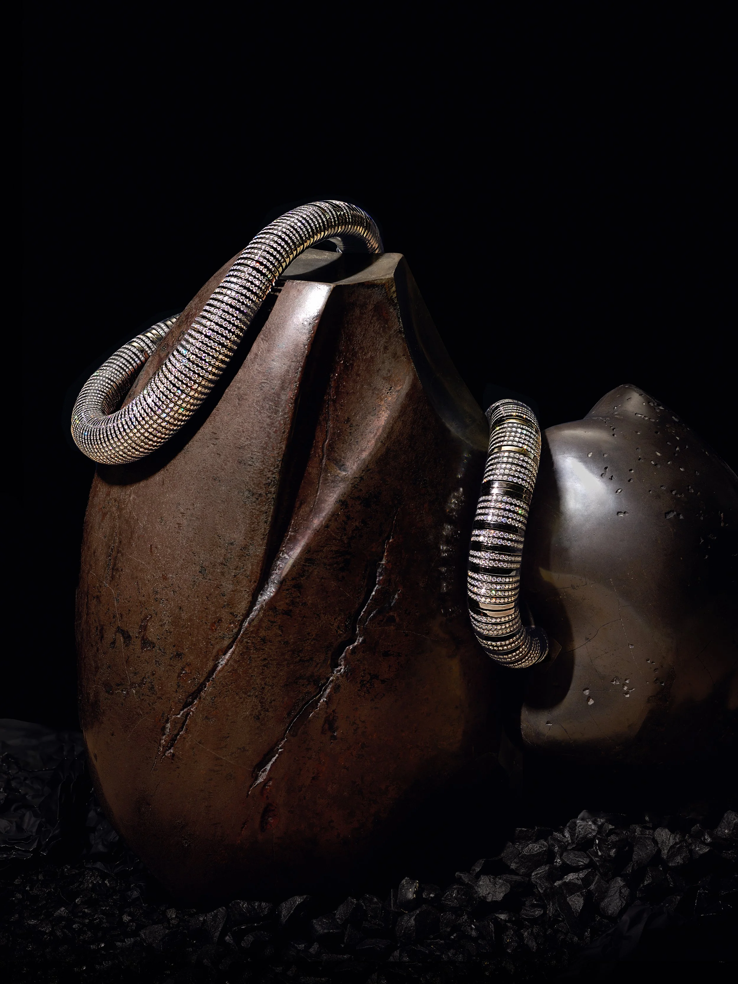 Two large stones with metal jewelry draped over them, black background.