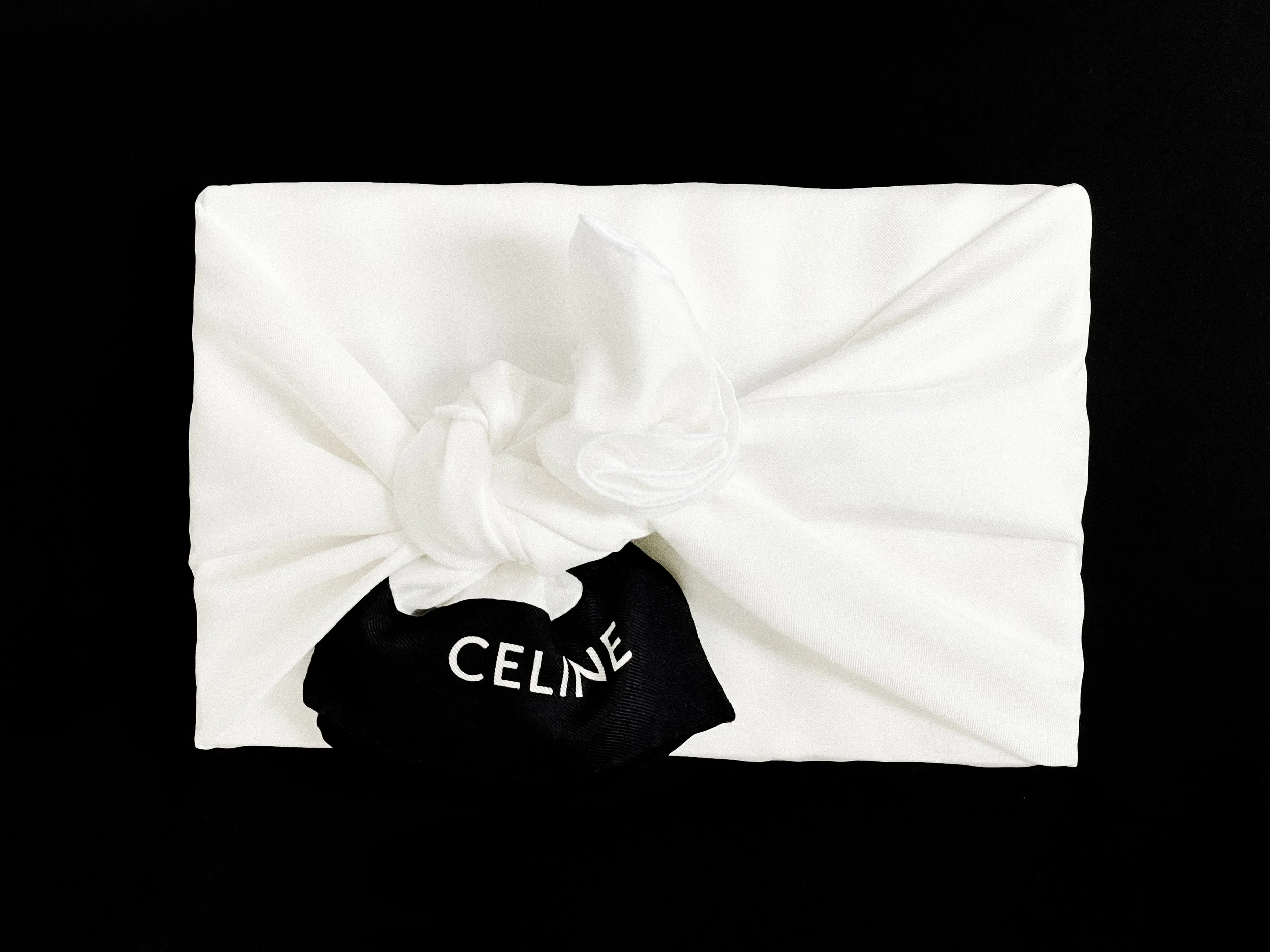 White wrapped gift box with a black ribbon tied in a bow, labeled 'CELINE', on a black background.