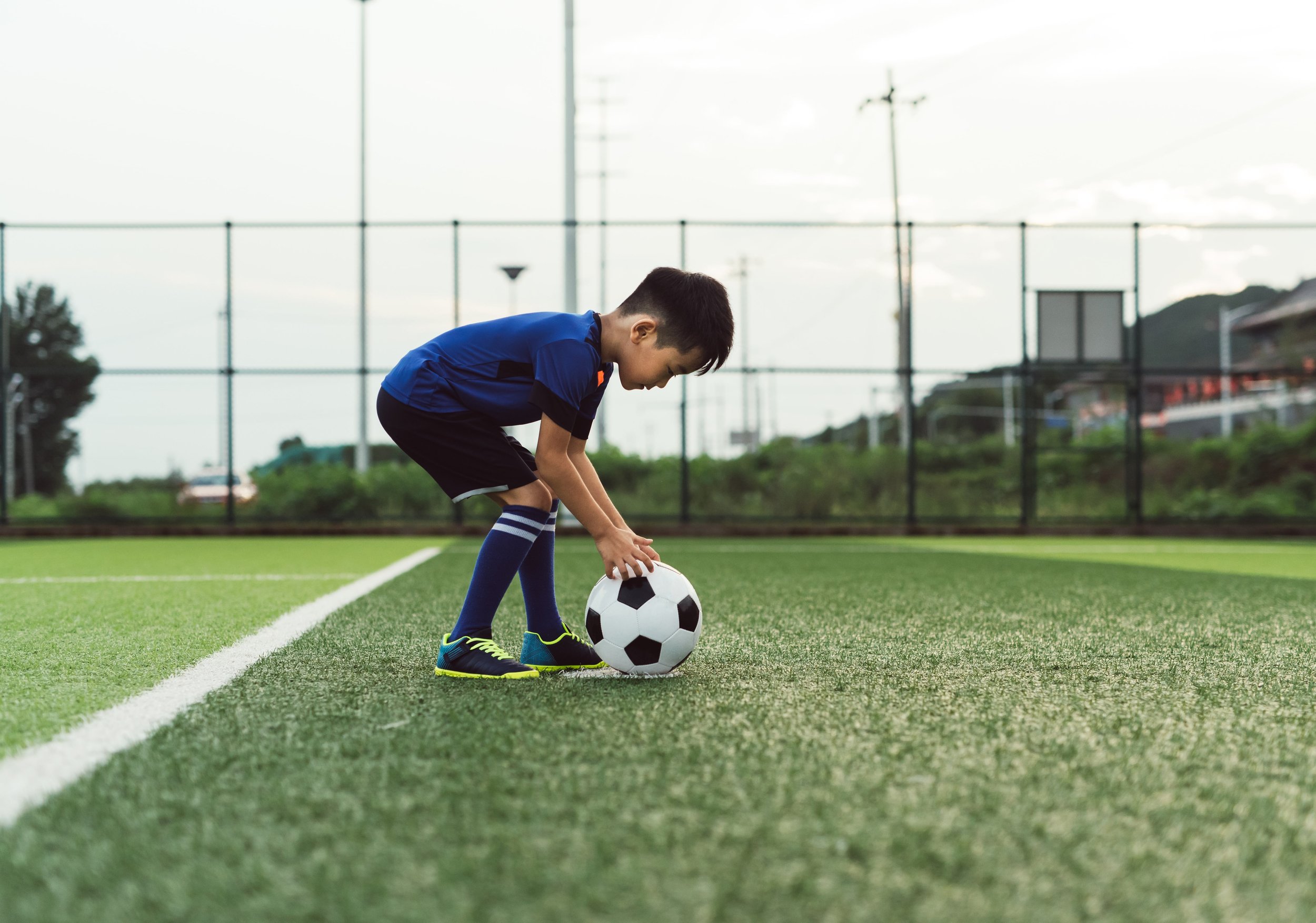 Niño pequeño asiático jugando fútbol en la cancha de juego