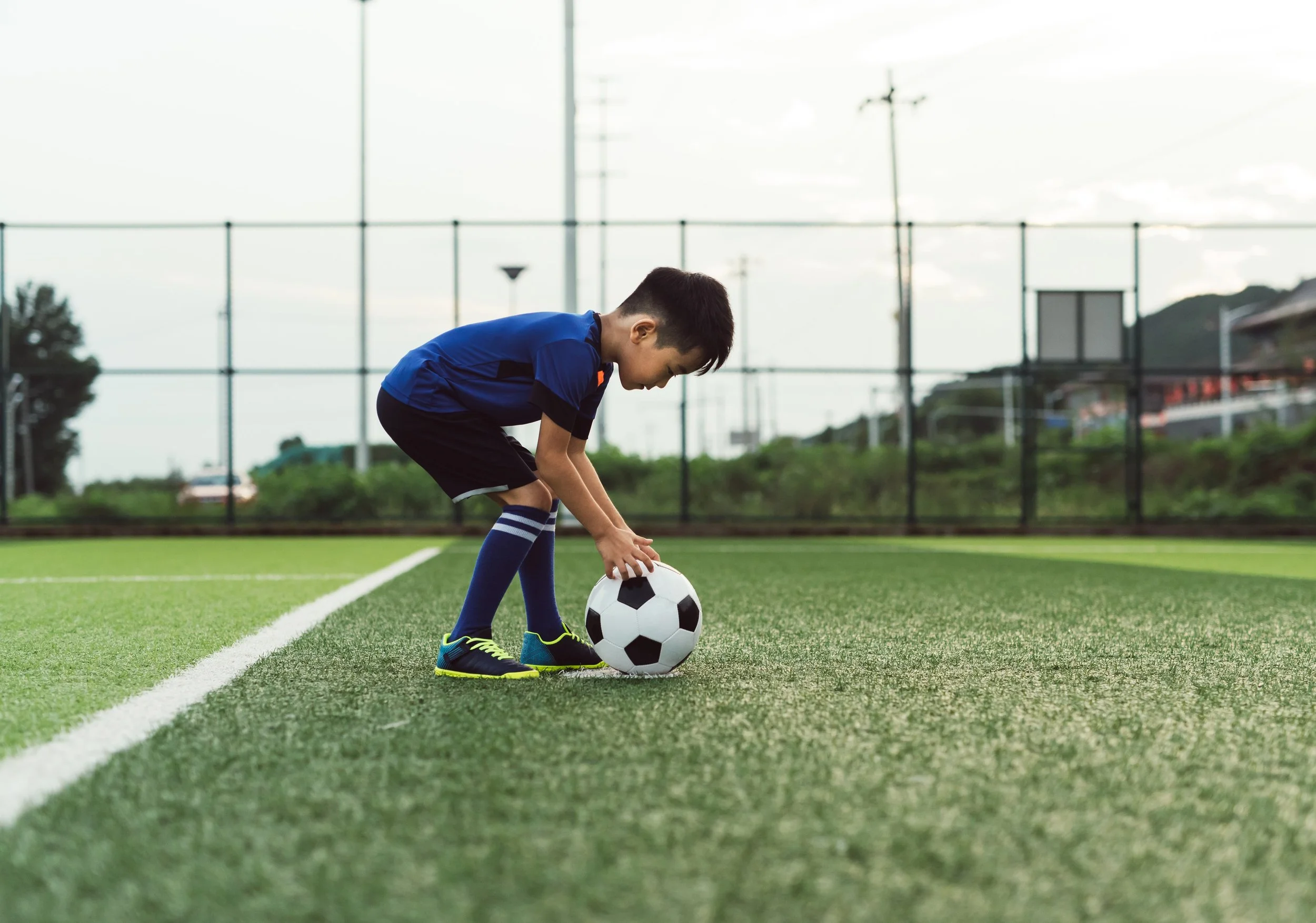 Asiatisches Kleinkind spielt Fußball auf dem Platz