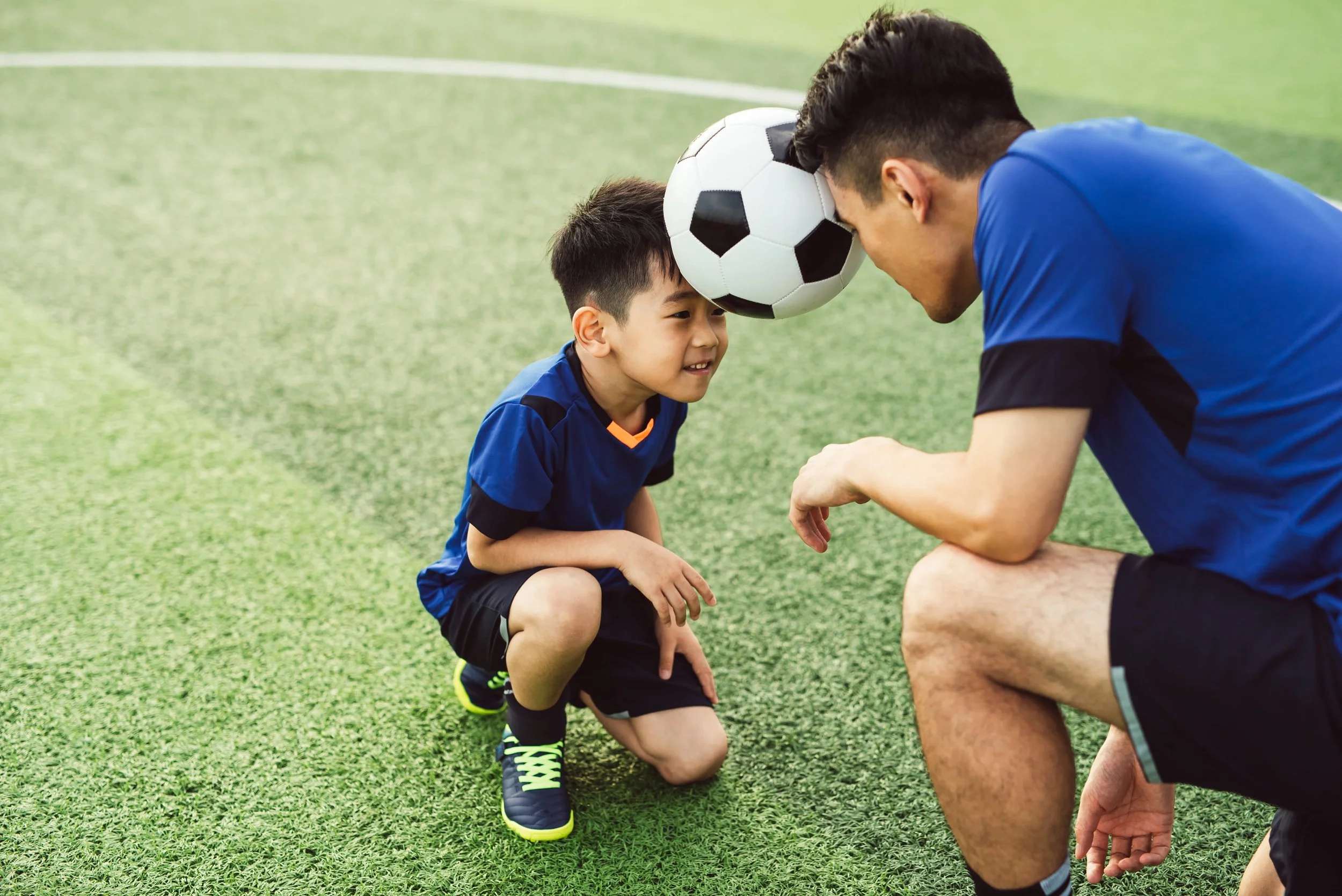 Ein junger asiatischer Vater und sein süßer Sohn spielen Fußball auf dem Sportplatz