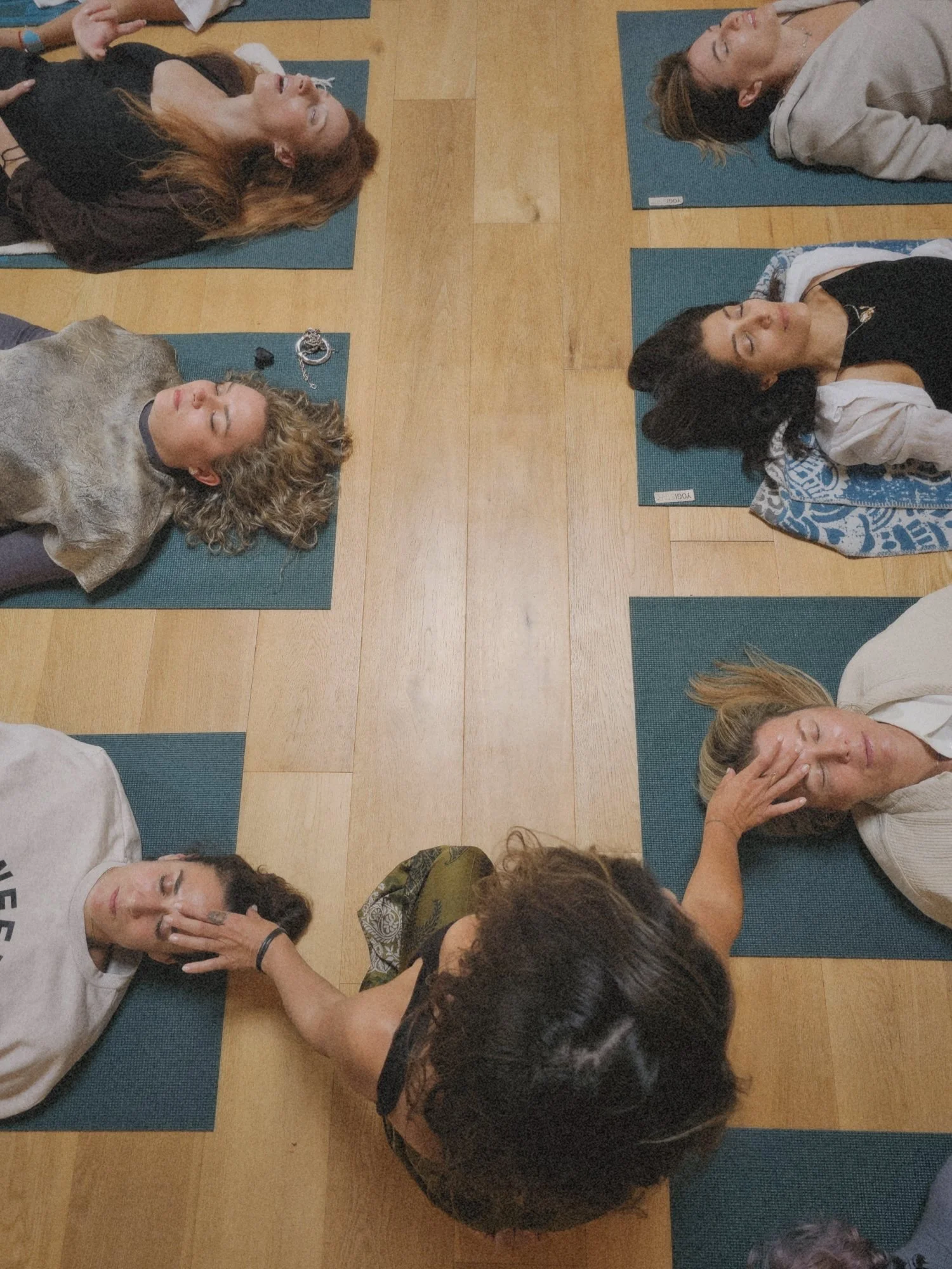 Grupo de personas haciendo yoga en posición de relajación en un suelo de madera con colchonetas.