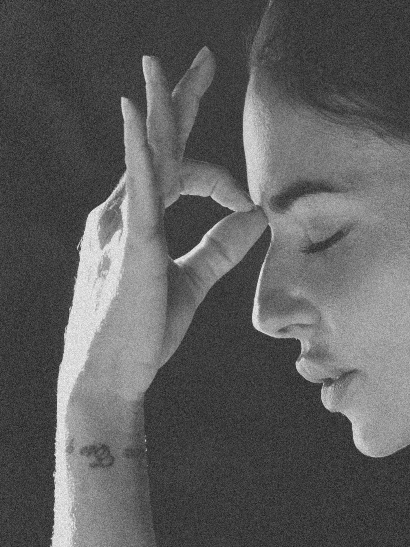 Retrato en blanco y negro de una mujer con los ojos cerrados, tocándose la frente con la mano izquierda