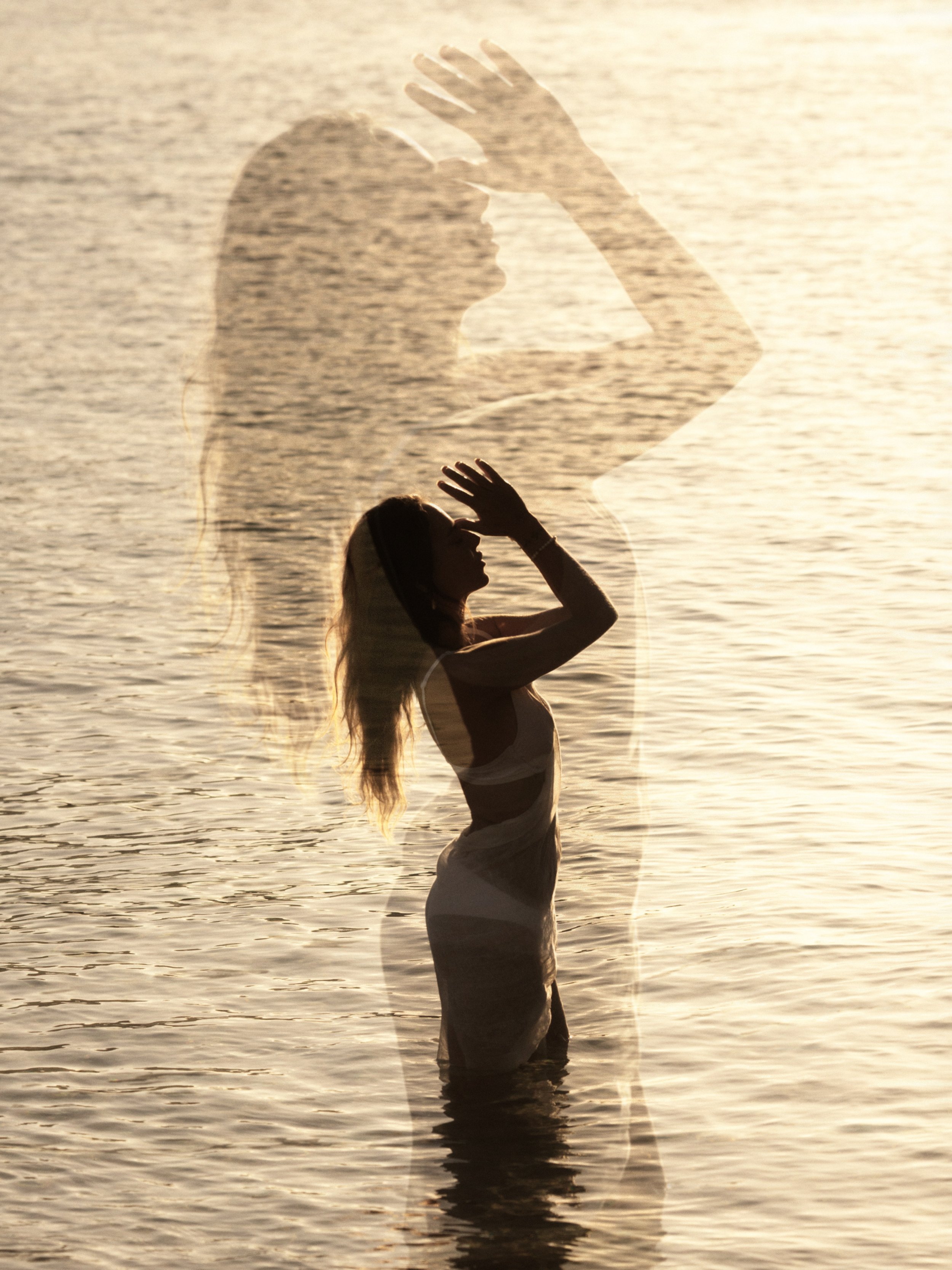 Silhouette de una mujer en el agua, con una superposición de su sombra en la misma escena durante el atardecer