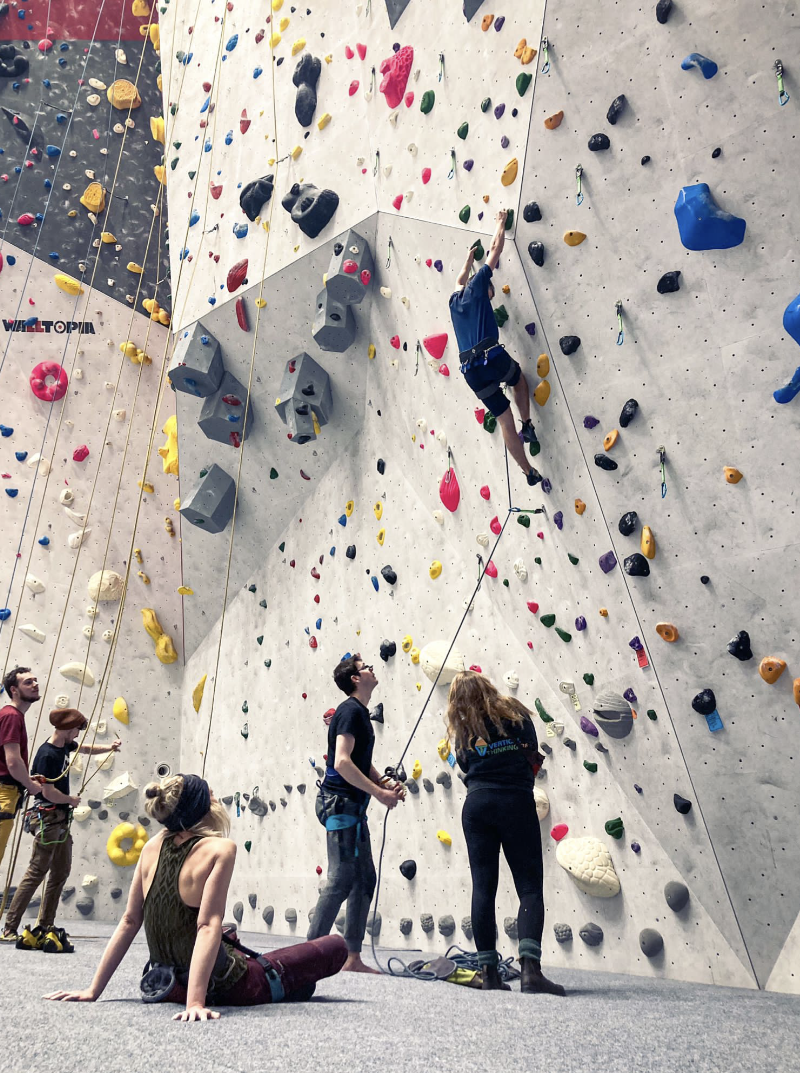 Een groep mensen die aan het klimmen is in een indoor klimhal met gekleurde klimwanden en klettergrepen.