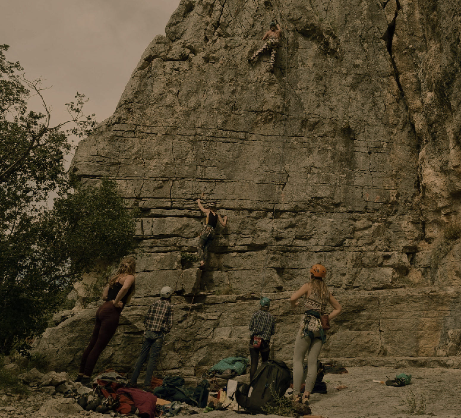 vrouw met klimuitrusting en helm staat op een rots bij een steile, rotsachtige muur in een berglandschap.