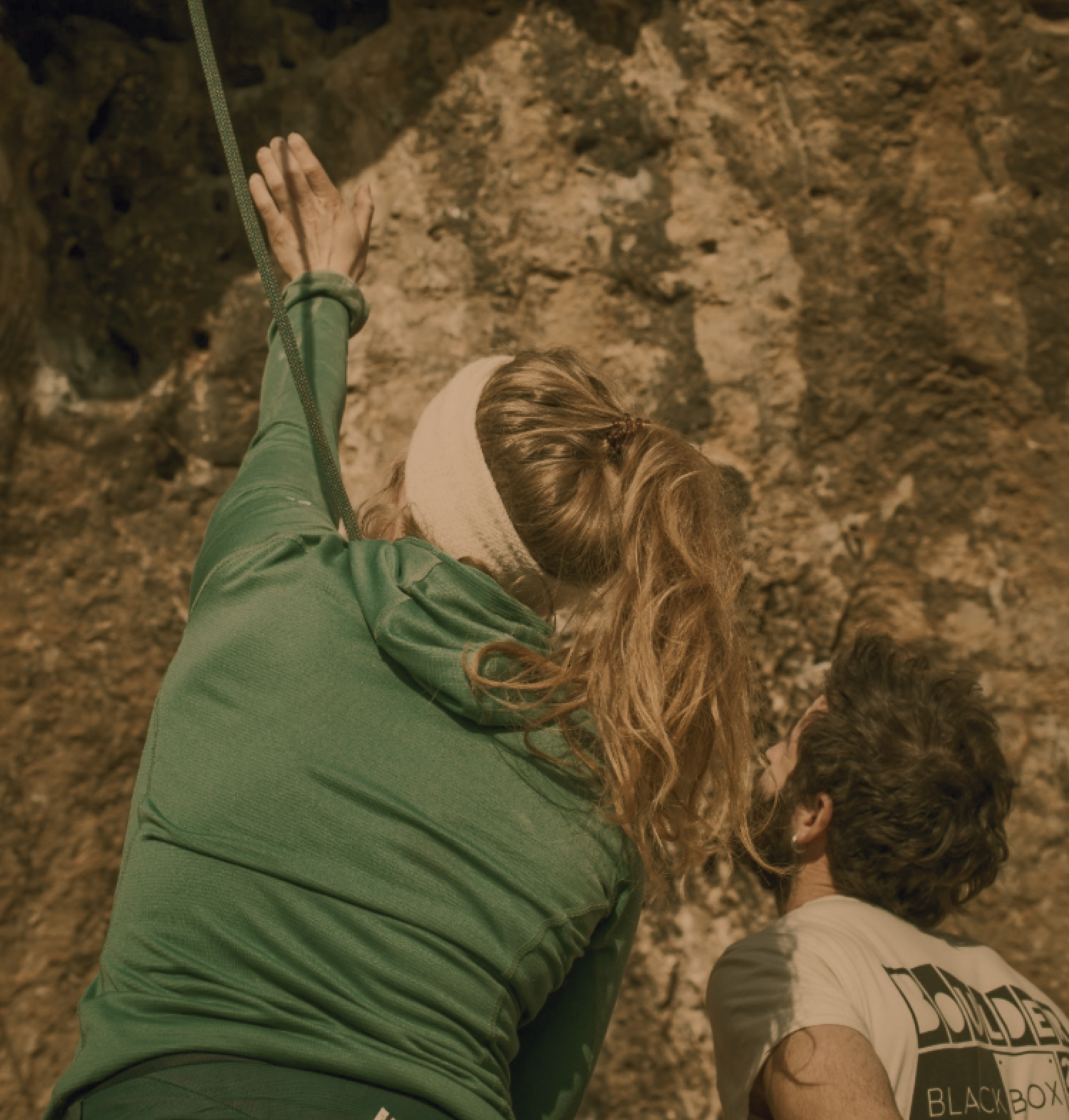 Klimmer in beschermende uitrusting op rotswand met uitzicht op diepe kloof en steile kliffen, omgeven door bomen.