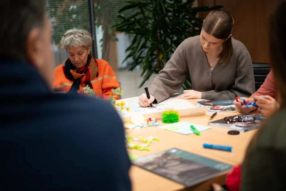 People sitting around a table working on arts and crafts, with colorful materials and papers in a well-lit room.