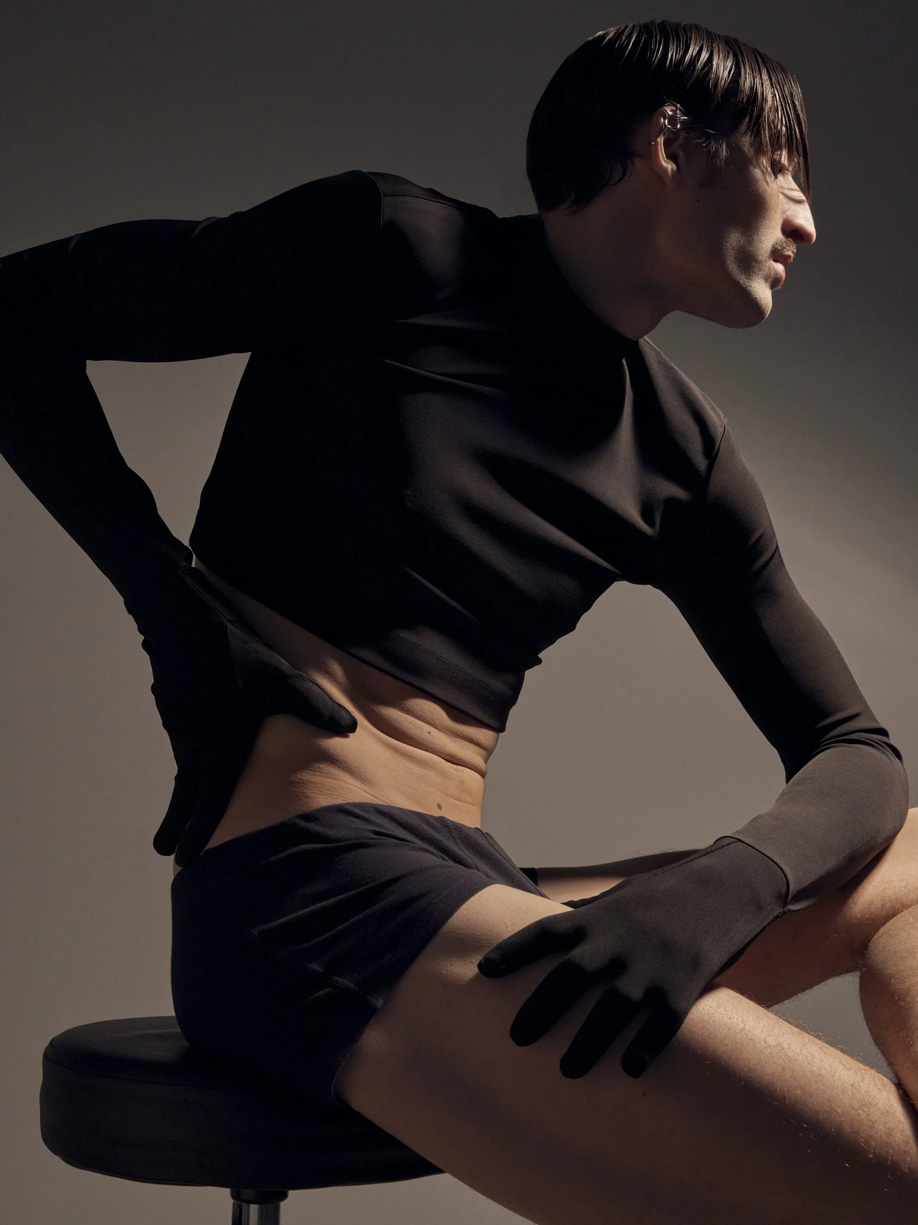 männliches Model in schwarzem Shirt, Slip und Handschuhen in Studio