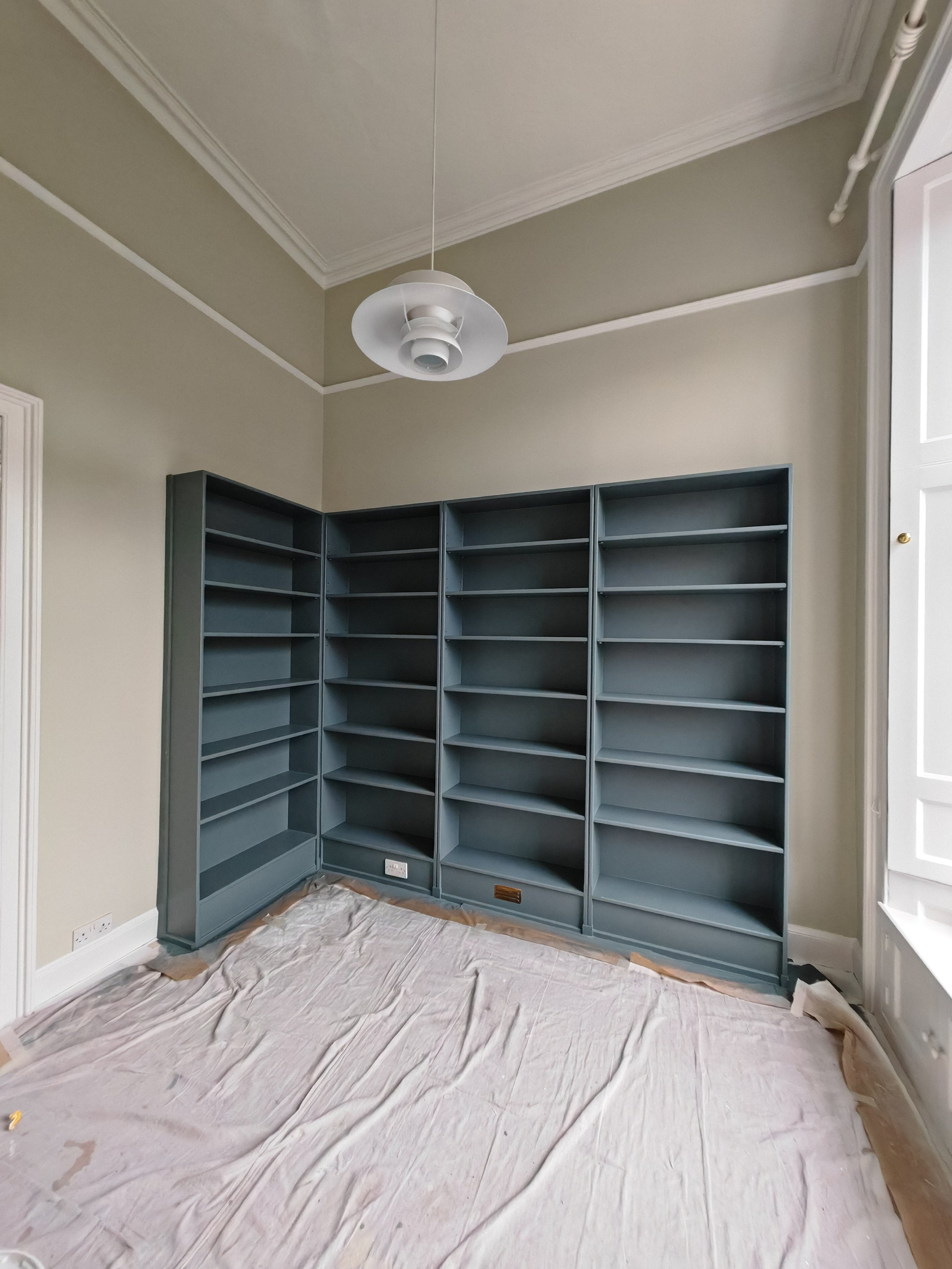Empty blue bookshelf in a room with beige walls, a ceiling light, and covered floor.
