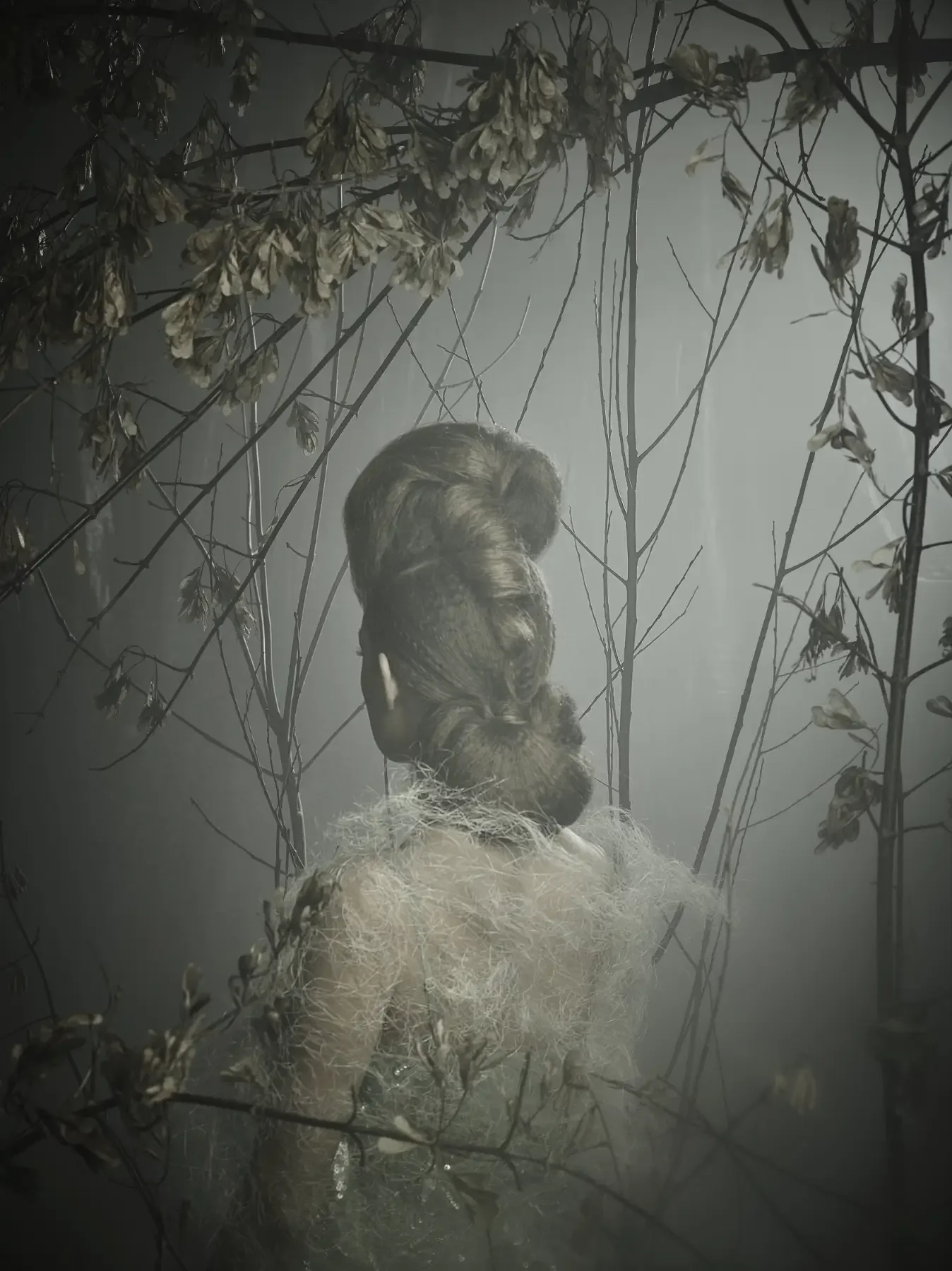 Rückansicht eines avantgardistischen Editorial-Hairstylings in nebliger Waldkulisse. Die skulpturale Frisur, feine textile Strukturen und kahle Äste erzeugen eine ruhige, mystische Fine-Art-Atmosphäre mit Garzareck-Charakter.