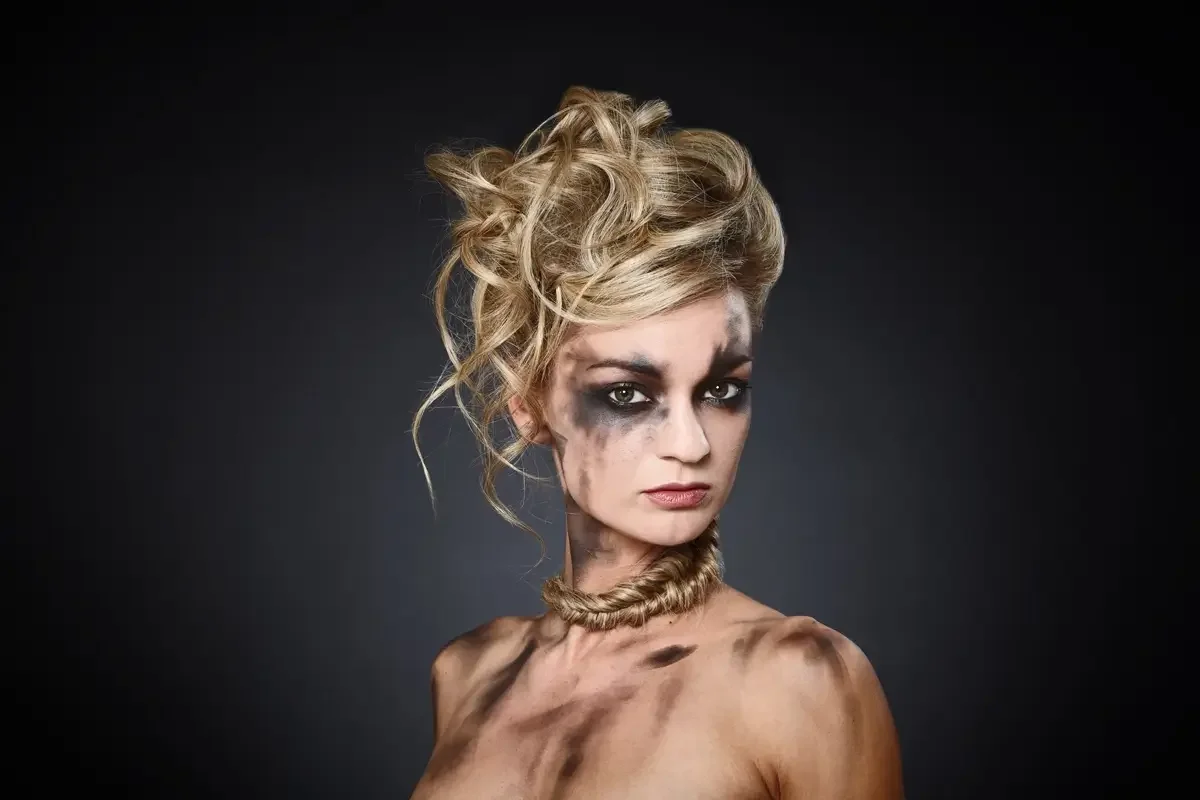 Avantgardistisches Beauty-Editorial mit blondem Messy-Updo, dramatischem schwarzem Augen-Make-up und geflochtenem Haar-Accessoire um den Hals. Garzareck Styling mit Fokus auf expressive Haut-, Haar- und Fashion-Inszenierung.