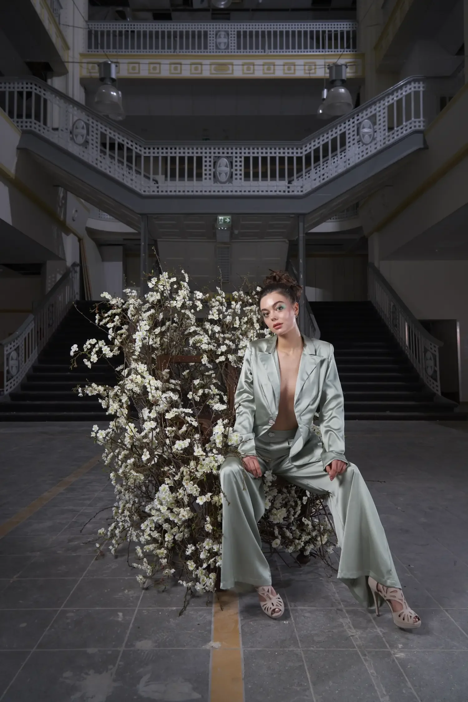 Editorial-Fashionfotografie aus der Serie „Botanical Avantgarde“ von Garzareck mit Model im mintfarbenen Satinanzug vor blühenden Zweigen im historischen Stadtbad Halle.