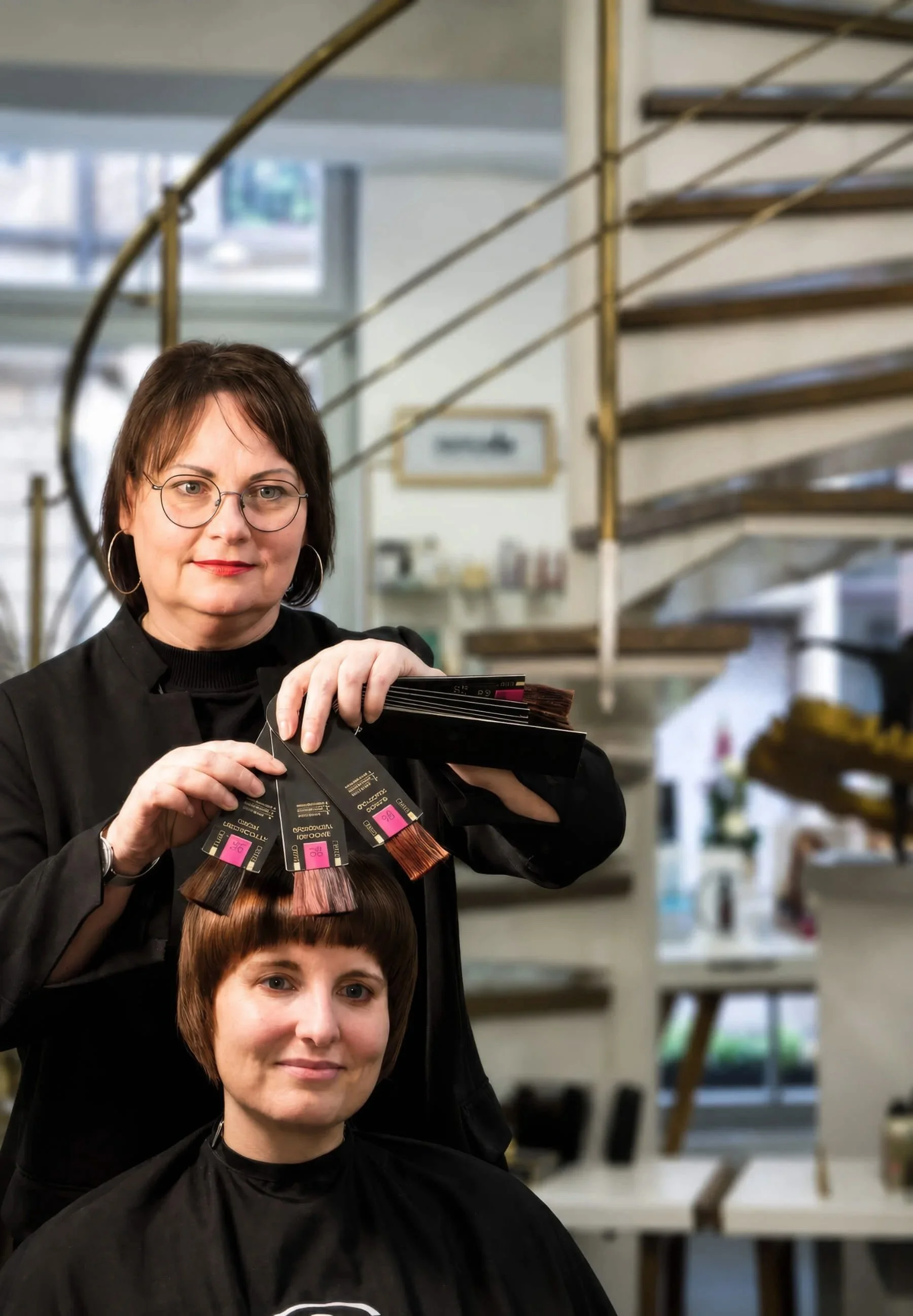 Friseurmeisterin vergleicht professionelle Haarfarbmuster mit dem Haarton einer Kundin während einer individuellen Farbberatung bei Garzareck in Halle (Saale).