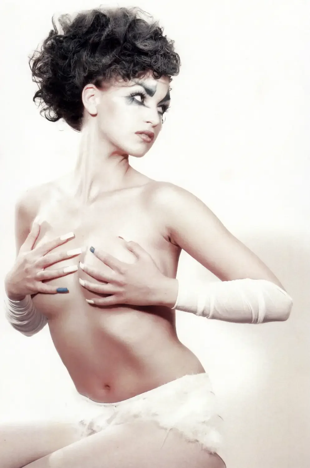 Avantgarde-Fashion-Porträt mit grafischem Augen-Make-up, lockiger Hochsteckfrisur und minimalistischer Studioästhetik.