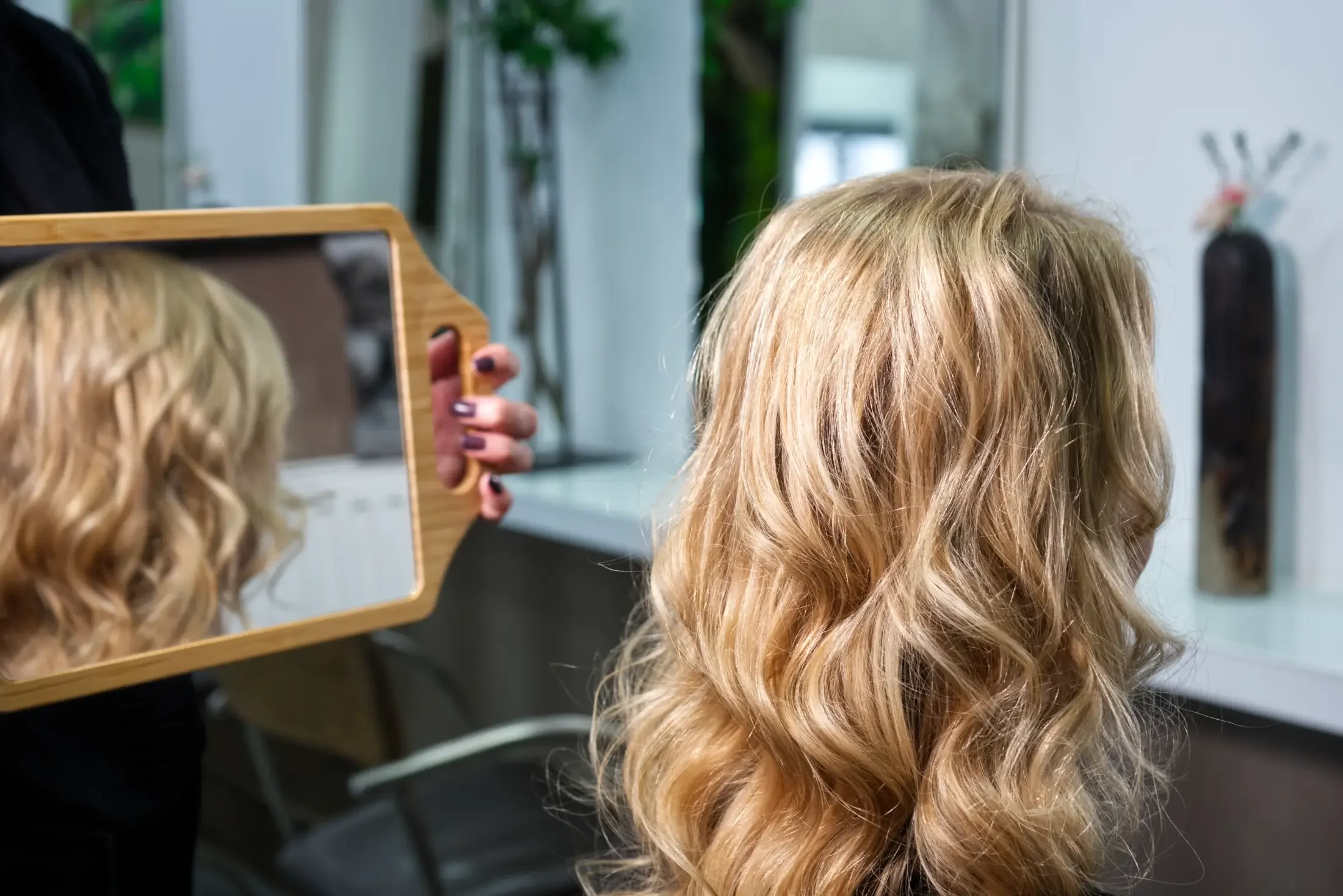 Das Ergebnis einer Great Lengths Haarverlängerung mit langen, blonden Locken. Die Kundin betrachtet ihre natürliche Haarfülle im Spiegel nach der Behandlung bei Garzareck in Halle (Saale).