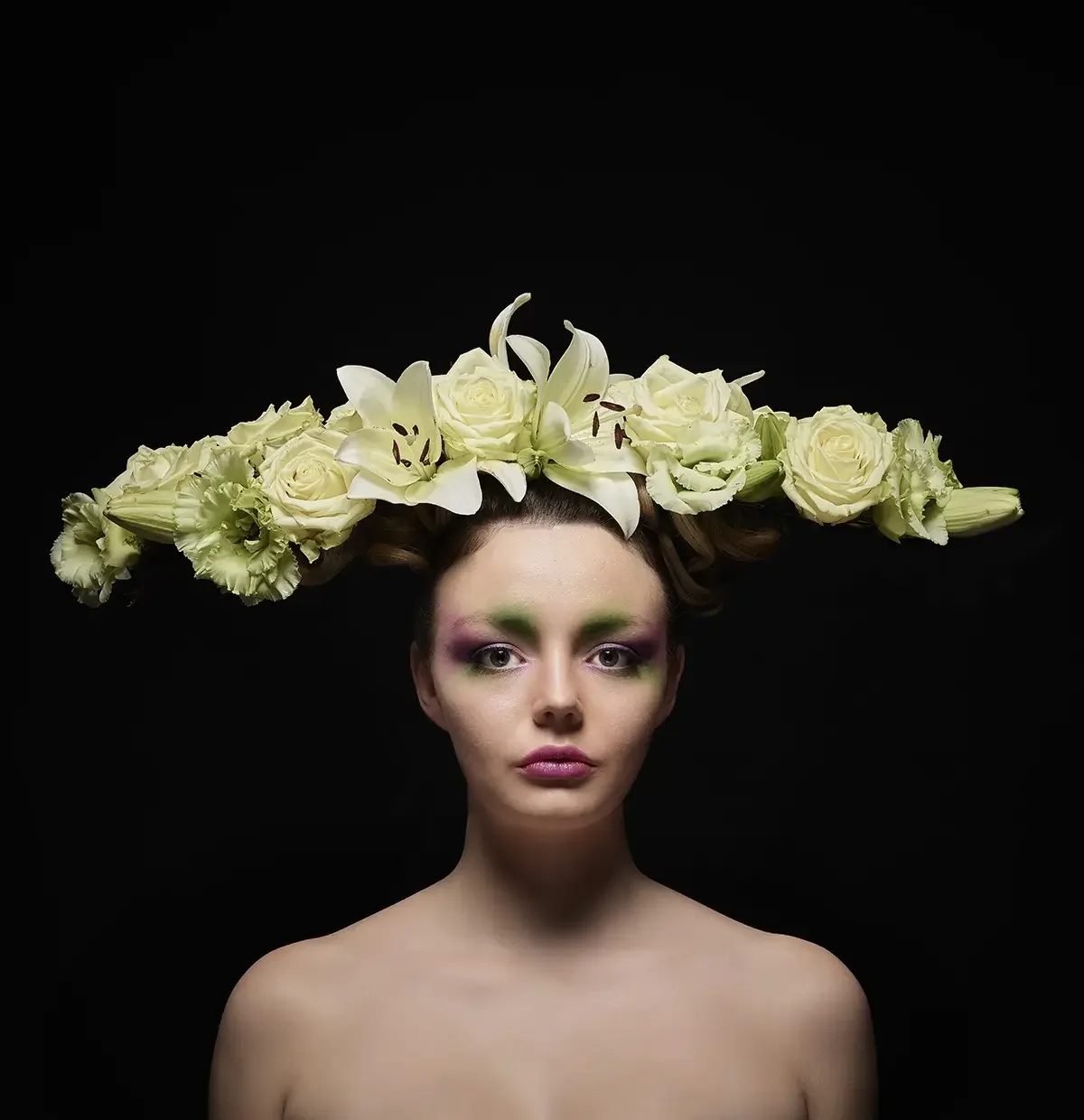 Studio-Avantgarde-Porträt mit floralem Kopfschmuck aus weißen Lilien und Rosen vor schwarzem Hintergrund aus der Serie „Verwurzelt schön“.