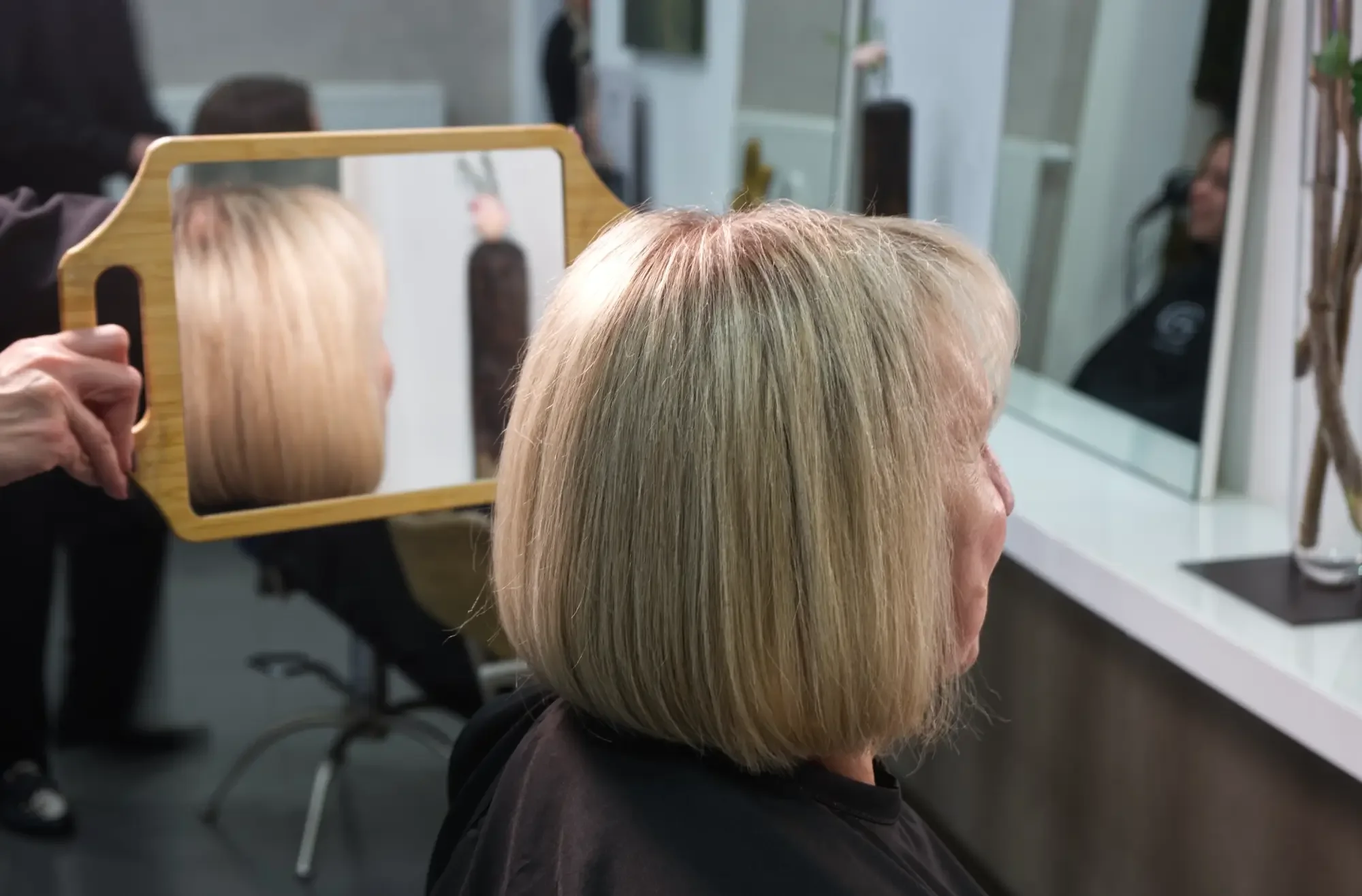 Ergebnis einer Great Lengths Haarverdichtung mit natürlich mehr Fülle und Volumen. Die Kundin betrachtet ihre neue Frisur im Handspiegel und das harmonische, nahtlose Ergebnis der Haarverdichtung bei Garzareck Halle (Saale).