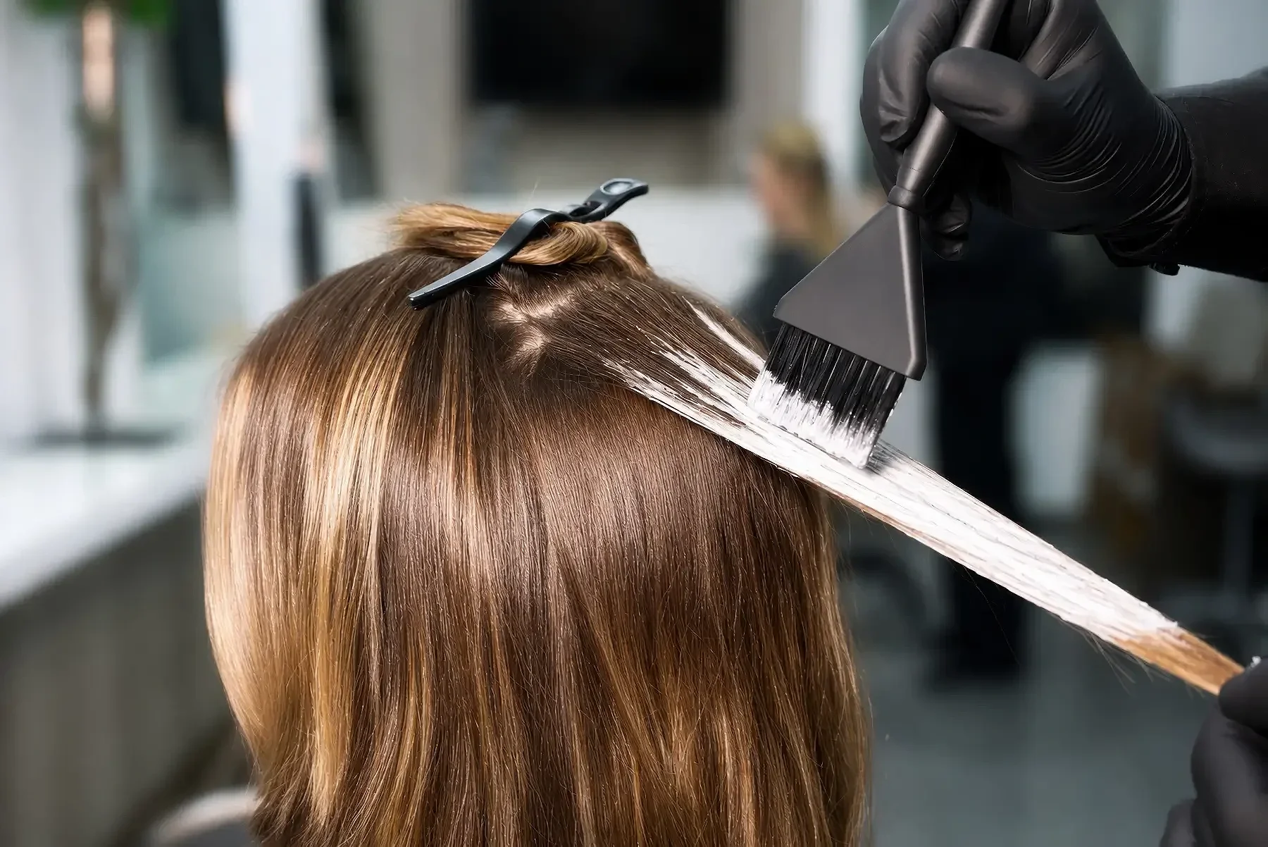 Friseurin trägt Haarfarbe auf die Haare eines Kunden auf, mit schwarzer Handschuhen, in einem Friseursalon.