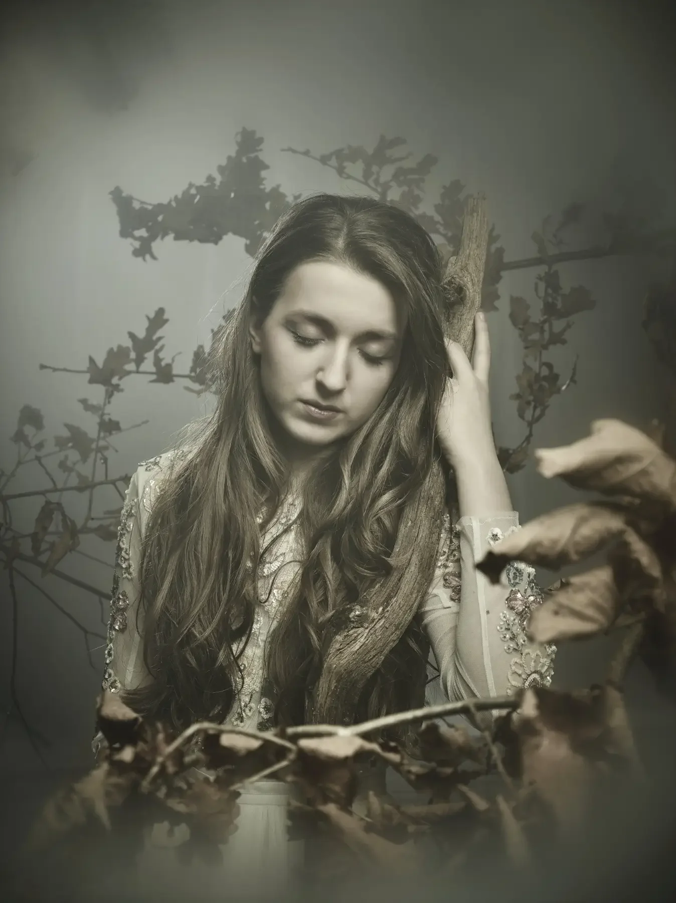 Melancholisches Fine-Art-Porträt einer jungen Frau mit langem Haar und besticktem Kleid in nebliger Waldszene. Verwachsene Äste, weiches Licht und natürliche Texturen erzeugen eine ruhige, cineastische Garzareck-Stimmung.
