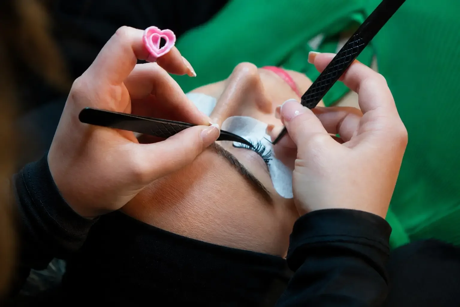 Feine Wimpernextensions werden mit zwei Präzisionspinzetten einzeln an den Naturwimpern angebracht, um die Wimpern dauerhaft zu verlängern und zu verdichten.