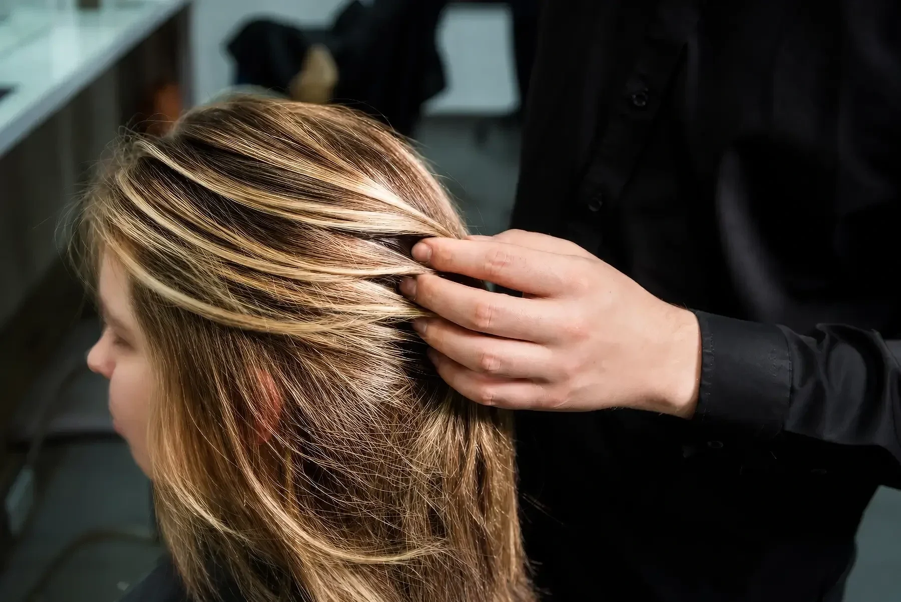 Friseurhand streift durch blondes Balayage-Haar mit feinen Highlights und natürlichen Farbverläufen während einer Farbberatung bei Garzareck in Halle (Saale).