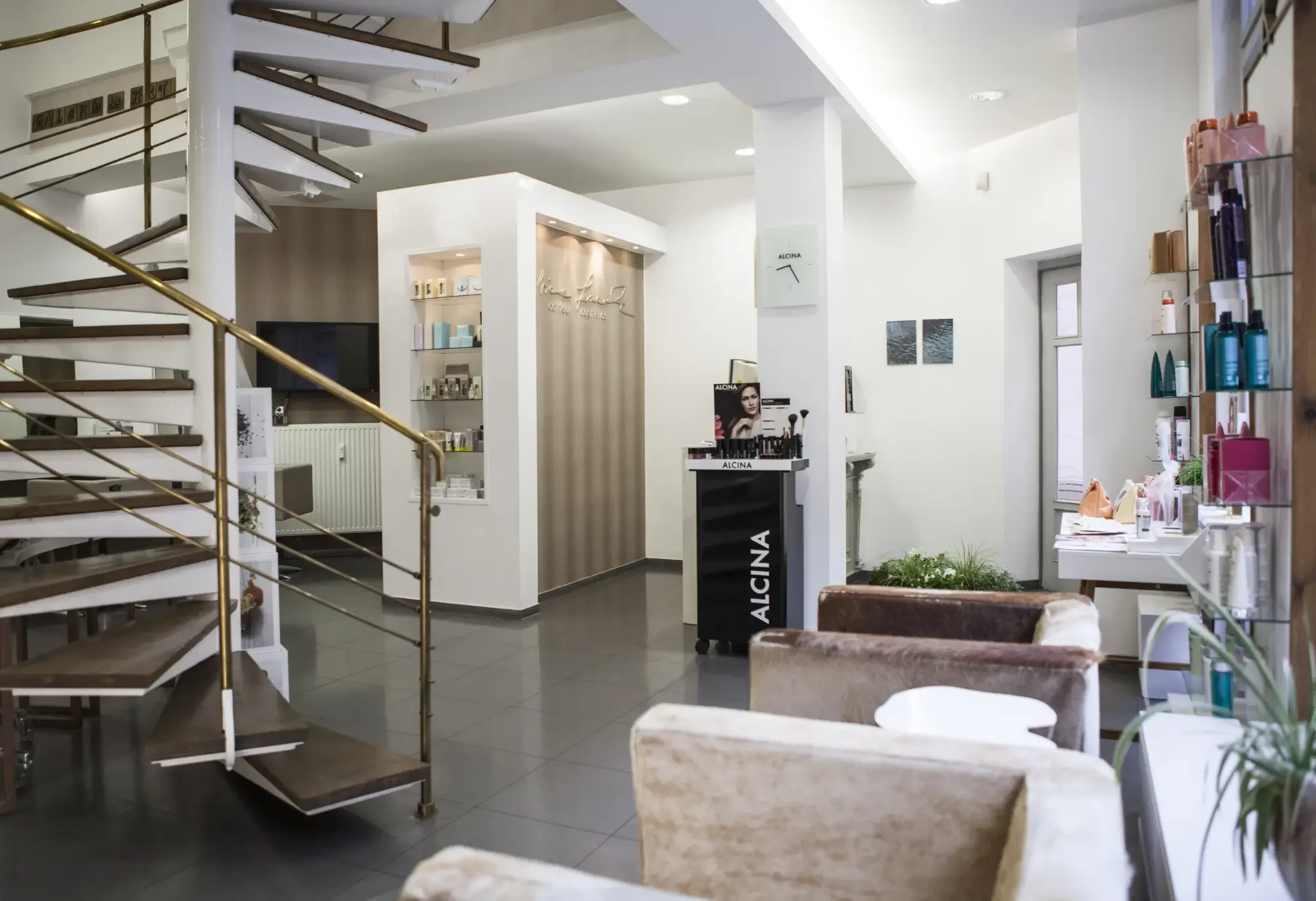 Helle Salonansicht mit Empfangsbereich, Wendeltreppe und Produktpräsentation bei Garzareck Coiffeur & Cosmetics in Halle (Saale).