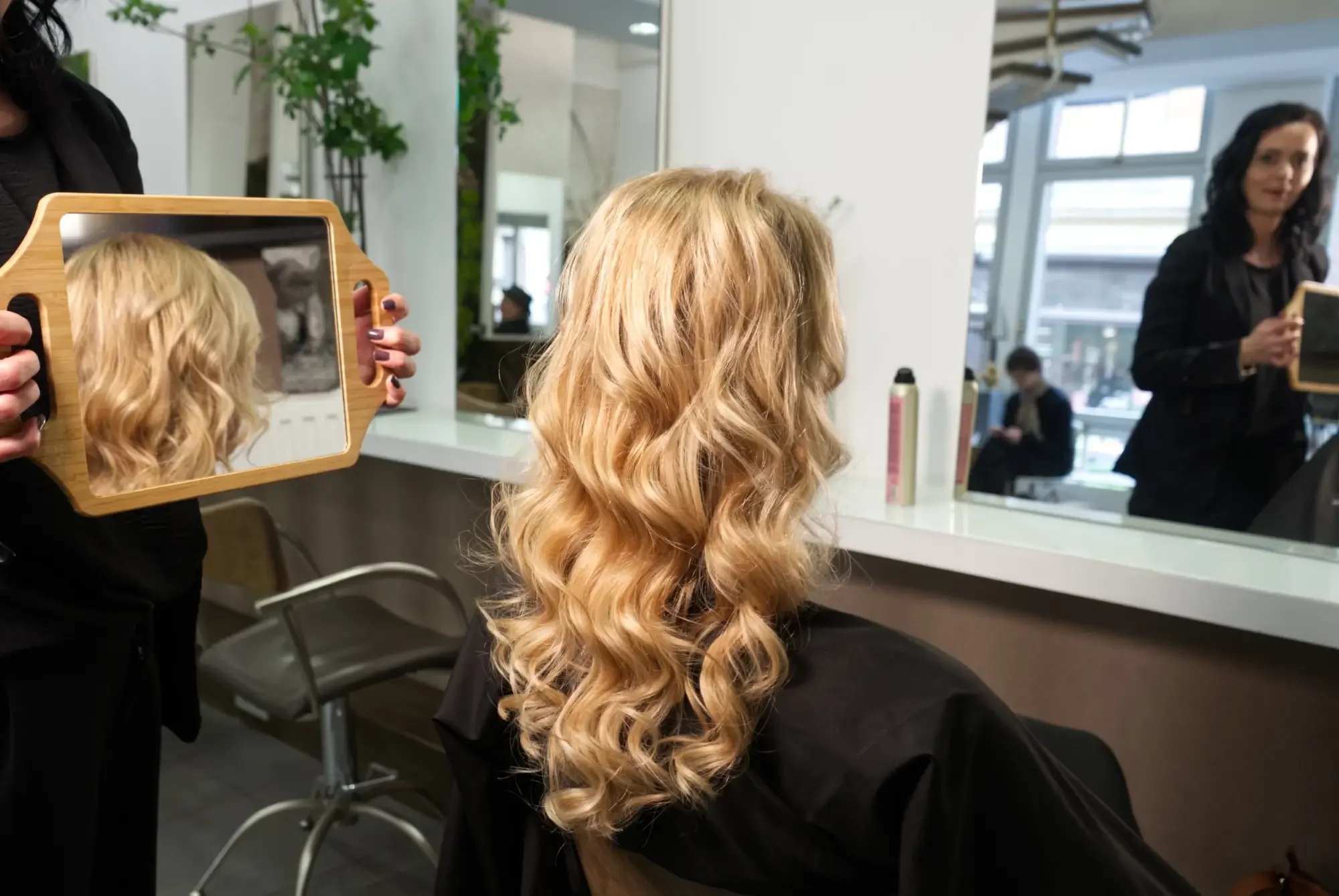 Das Ergebnis einer Great Lengths Haarverlängerung: Lange, blond gelockte Echthaare werden der Kundin im Handspiegel präsentiert. Natürliches Volumen und harmonische Haarlänge bei Garzareck in Halle (Saale).