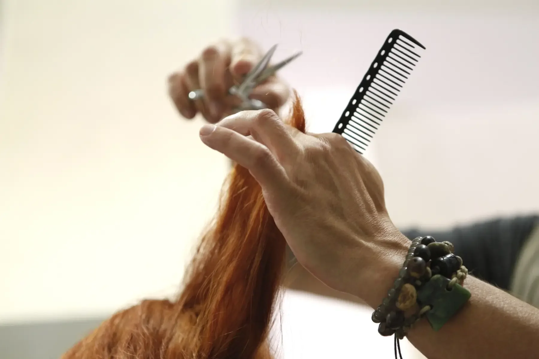 Hände eines Friseurs schneiden rötliches Haar mit Schere und Kamm, detailreiche Aufnahme handwerklicher Haarschneidearbeit bei Garzareck in Halle (Saale).