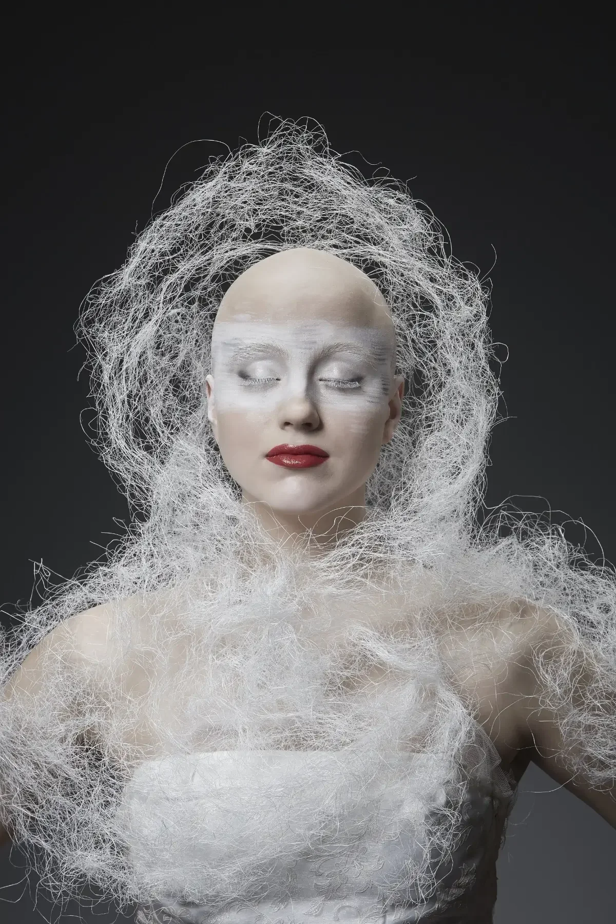 Zentral aufgenommenes Avantgarde-Porträt aus der Black-&-White-Fotoaktion mit geschlossenen Augen, weißer Gesichts- und Körperinszenierung, rotem Lippenakzent und ruhiger Ausstrahlung vor dunklem Hintergrund bei Garzareck in Halle (Saale).