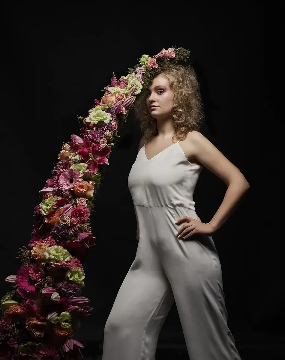 Studioporträt mit natürlicher Lockenfrisur und asymmetrischem Blumen-Headpiece aus Rosen, Lilien und Gerbera in einem floralen Avantgarde-Editorial von Garzareck Halle.