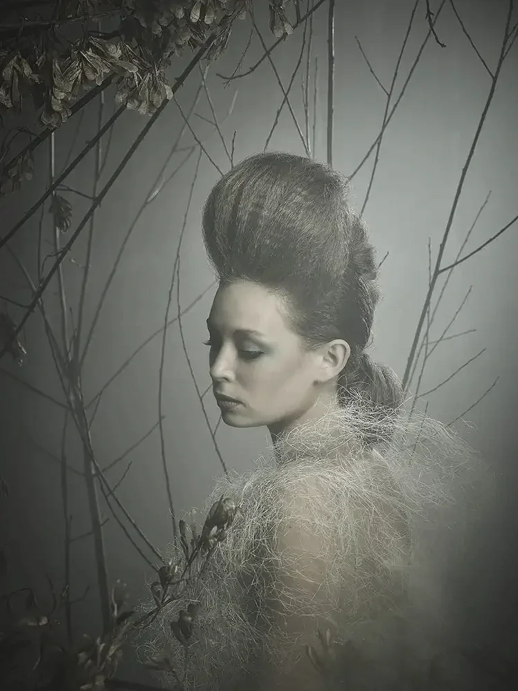 Model mit skulpturalem Editorial-Hairstyling in einer atmosphärischen Naturinszenierung aus Ästen und organischen Materialien der Serie „Verwurzelt schön“ von Garzareck.