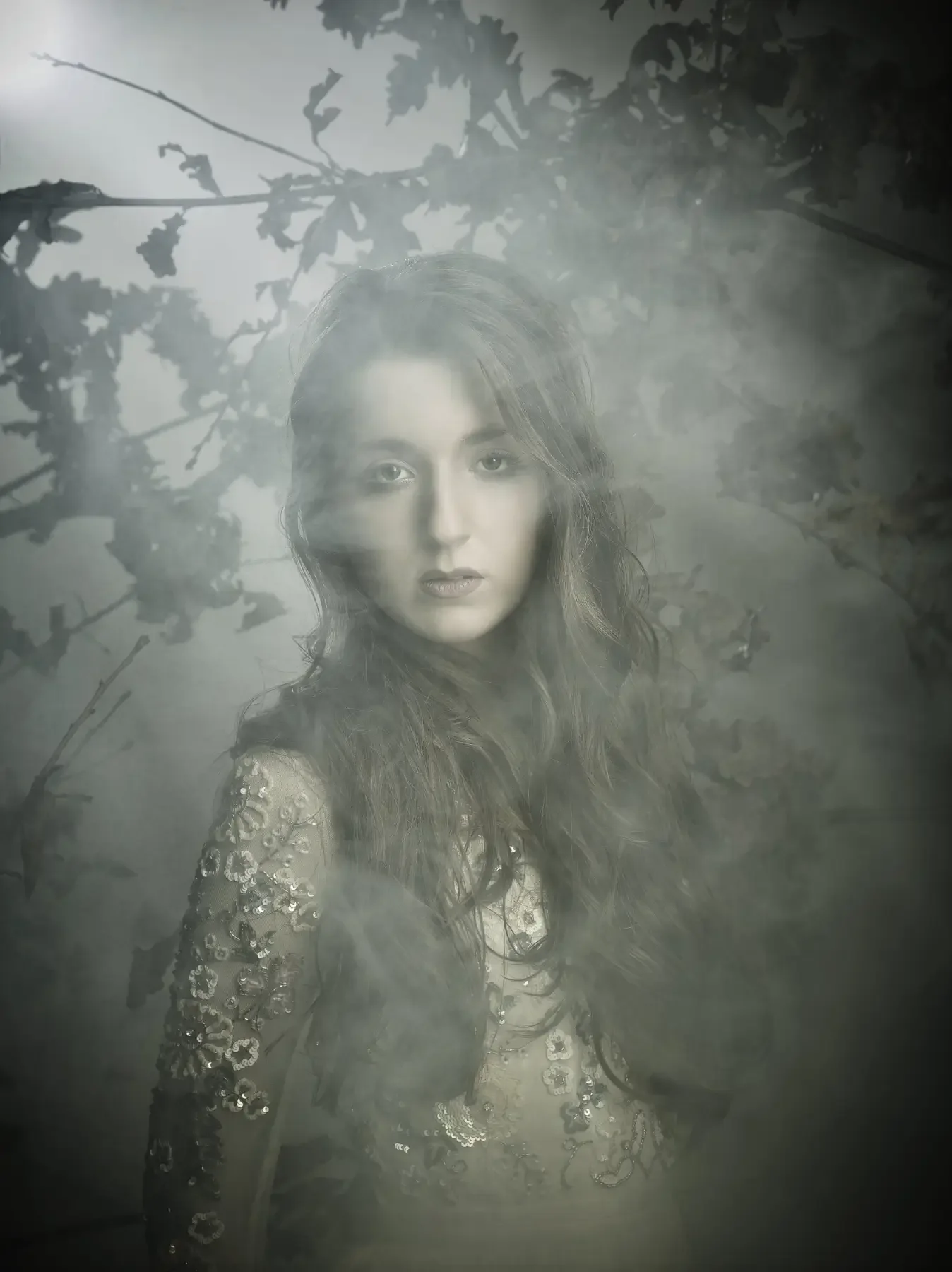 Atmosphärisches Editorial-Porträt einer jungen Frau mit langen Haaren und besticktem Kleid im Nebelwald. Diffuses Licht, organische Zweige und sanfte Naturtöne erzeugen eine ruhige, cineastische Garzareck-Stimmung.