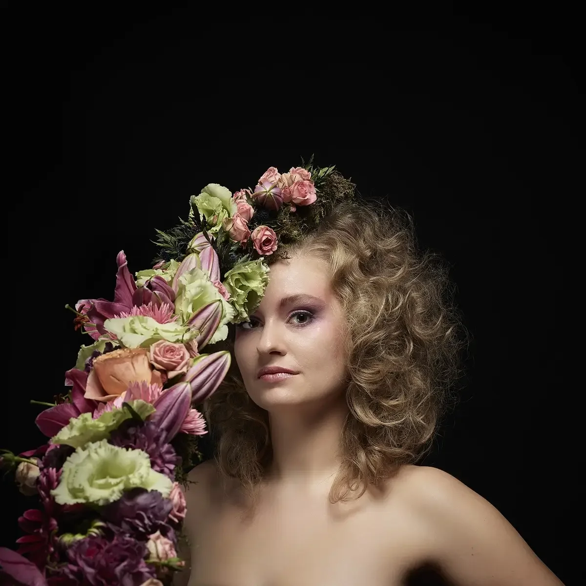 Studioporträt mit natürlicher Lockenfrisur und floralem Avantgarde-Headpiece aus Rosen und Lilien vor schwarzem Hintergrund bei Garzareck Friseur Halle.