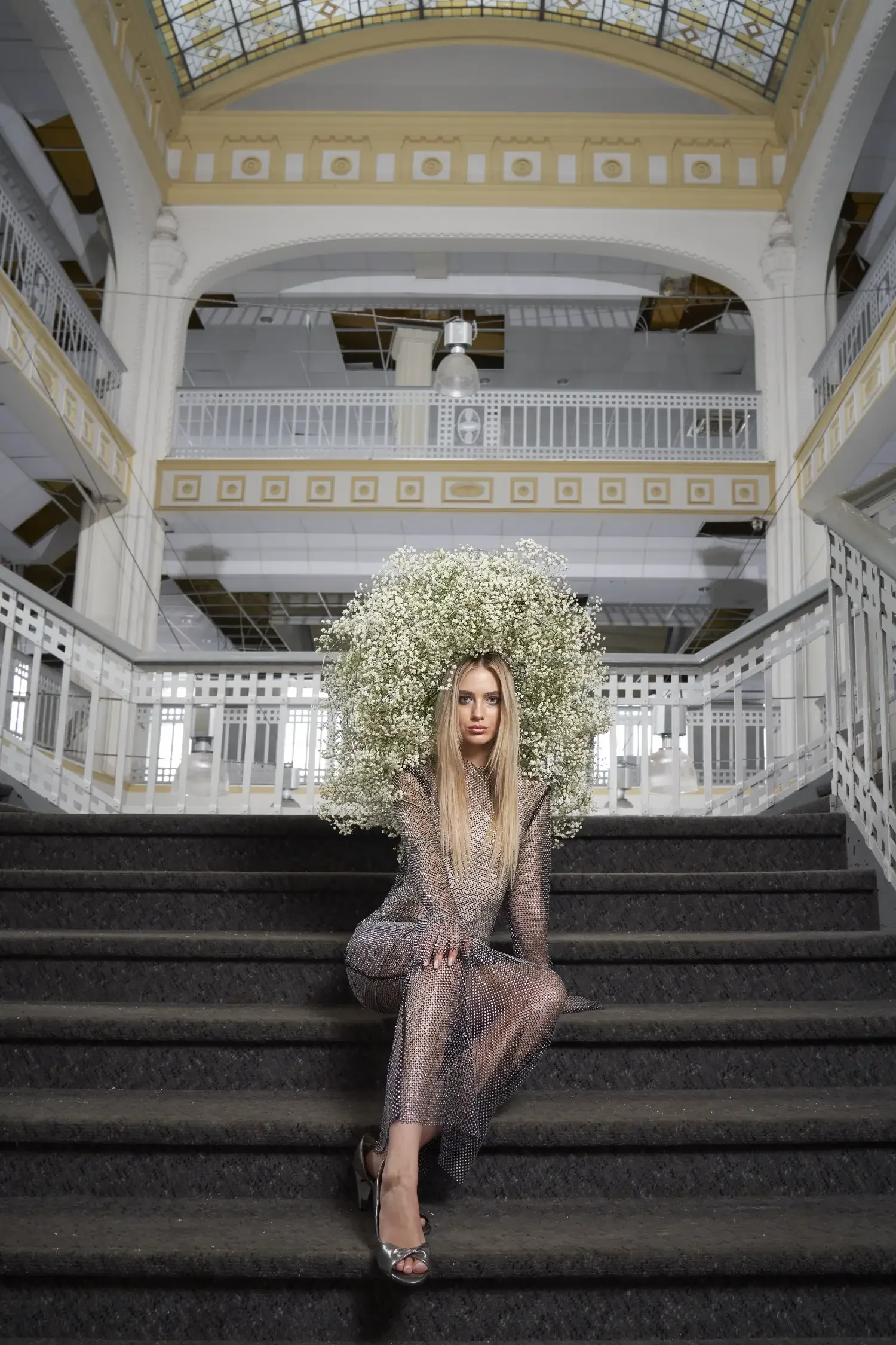 Fashion-Editorial im historischen Stadtbad Halle mit blondem Model auf monumentaler Treppe und opulentem Kopfschmuck aus weißen Schleierkraut-Blüten.