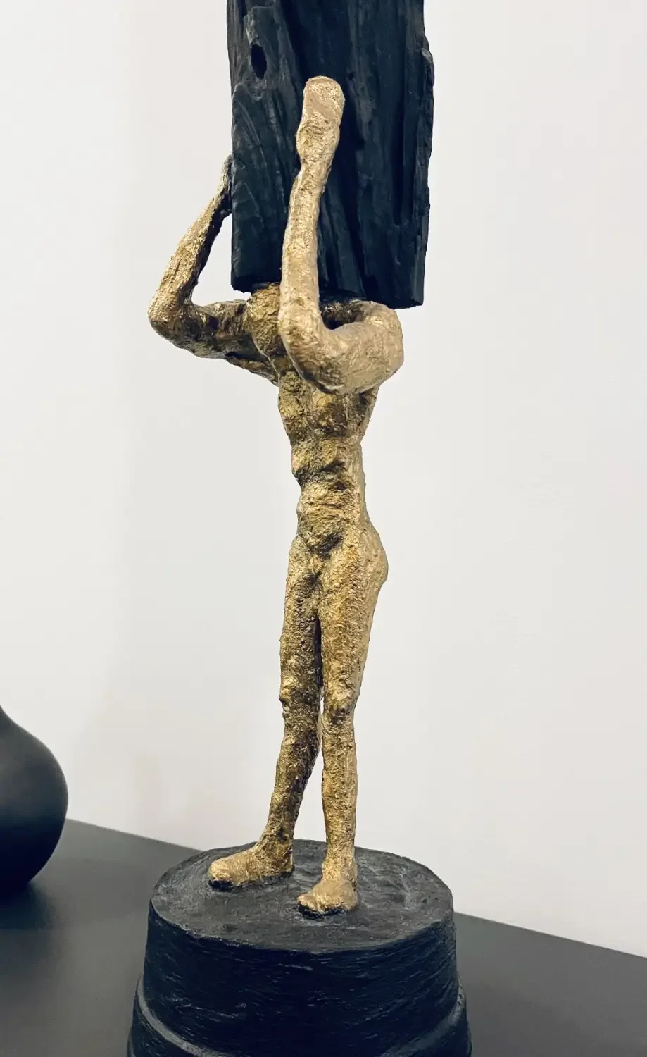 Skulptur von Andreas Walther Garzareck: Eine goldfarbene menschliche Figur trägt einen schwarzen Holzblock. Die plastische Arbeit vereint Skulptur, Objektkunst und natürliche Materialien.
